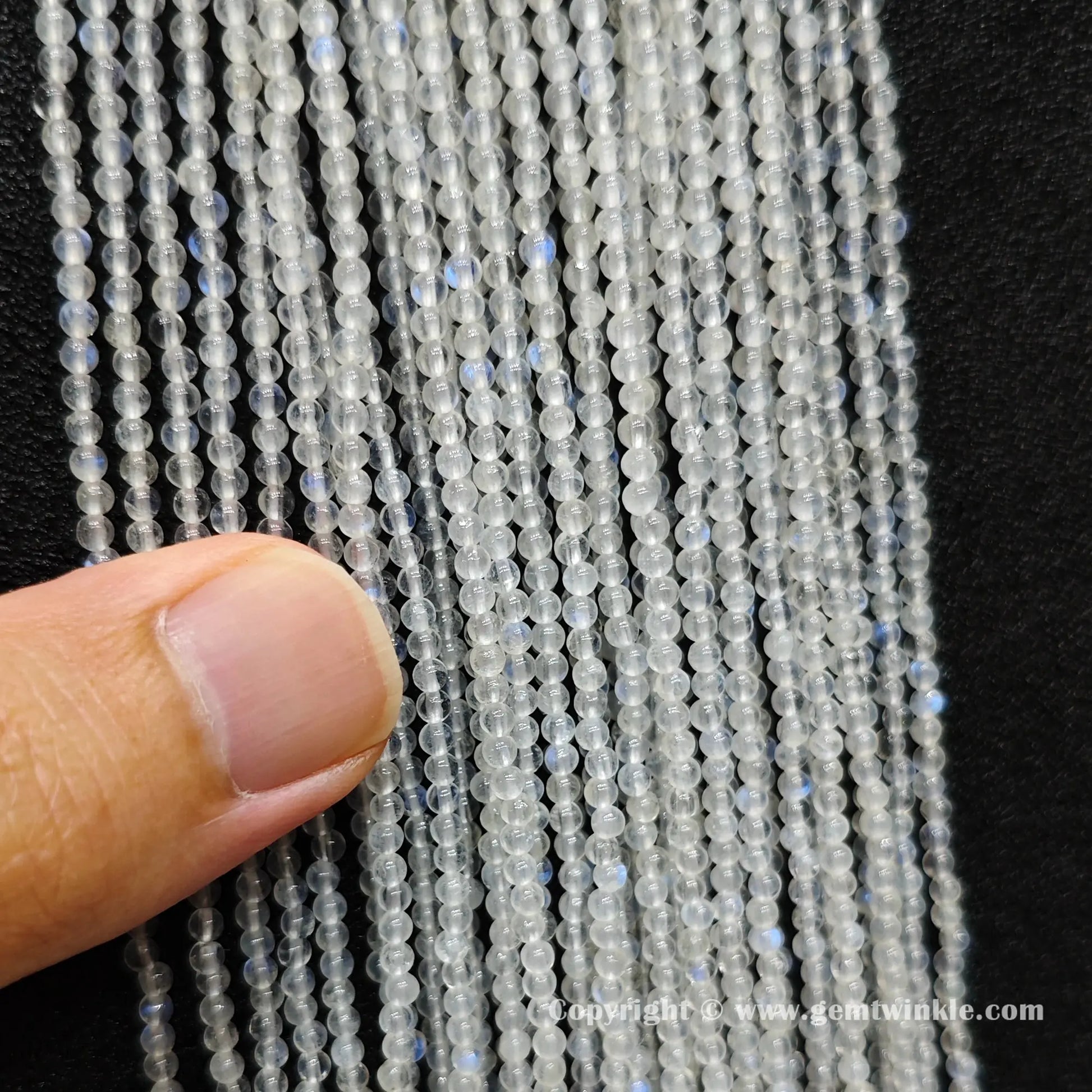 Close up view of 2mm micro blue flash moonstone seed beads inspected on hand for optical sheen preview