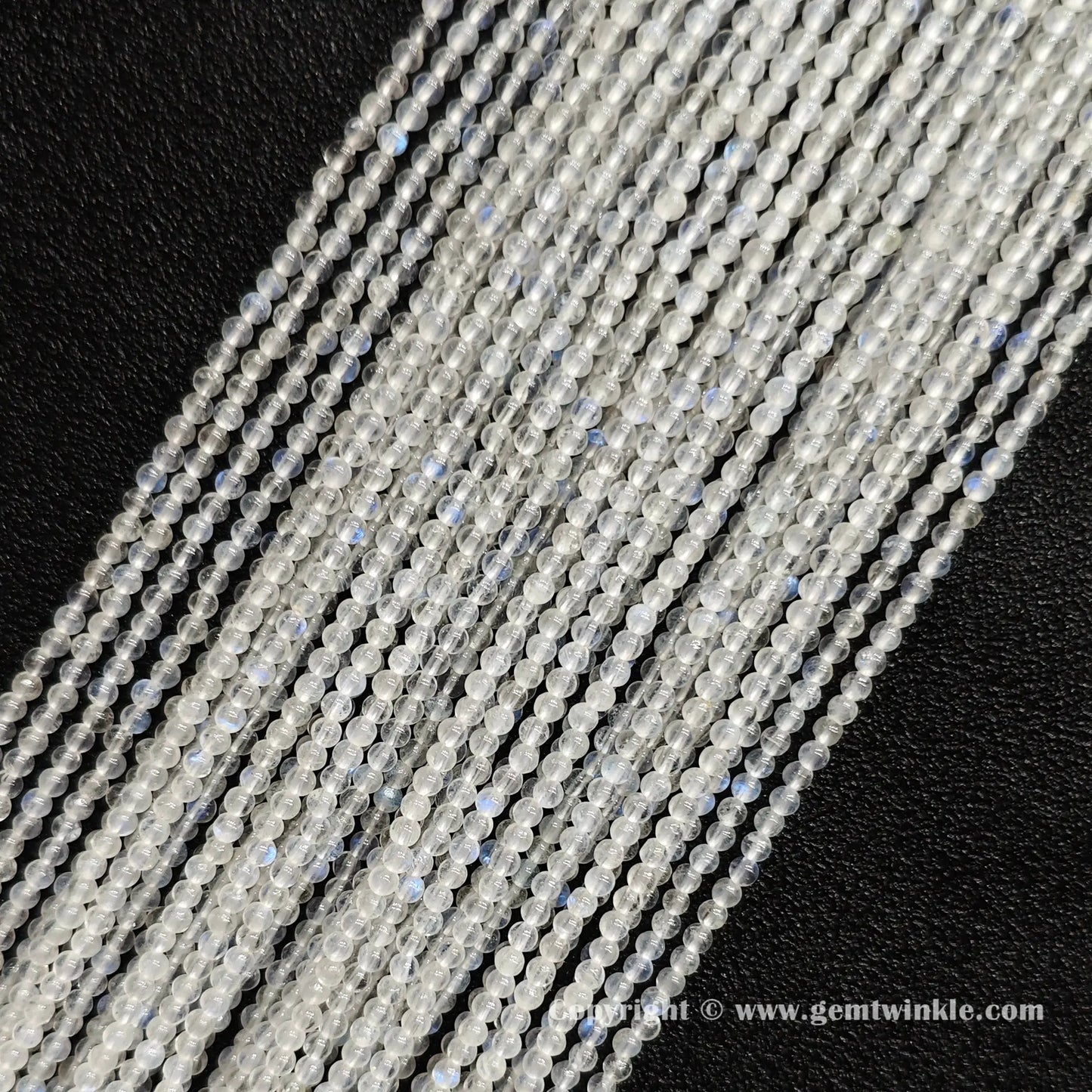 Angled view of 2mm micro blue flash moonstone seed bead strands laid parallel on dark textured surface
