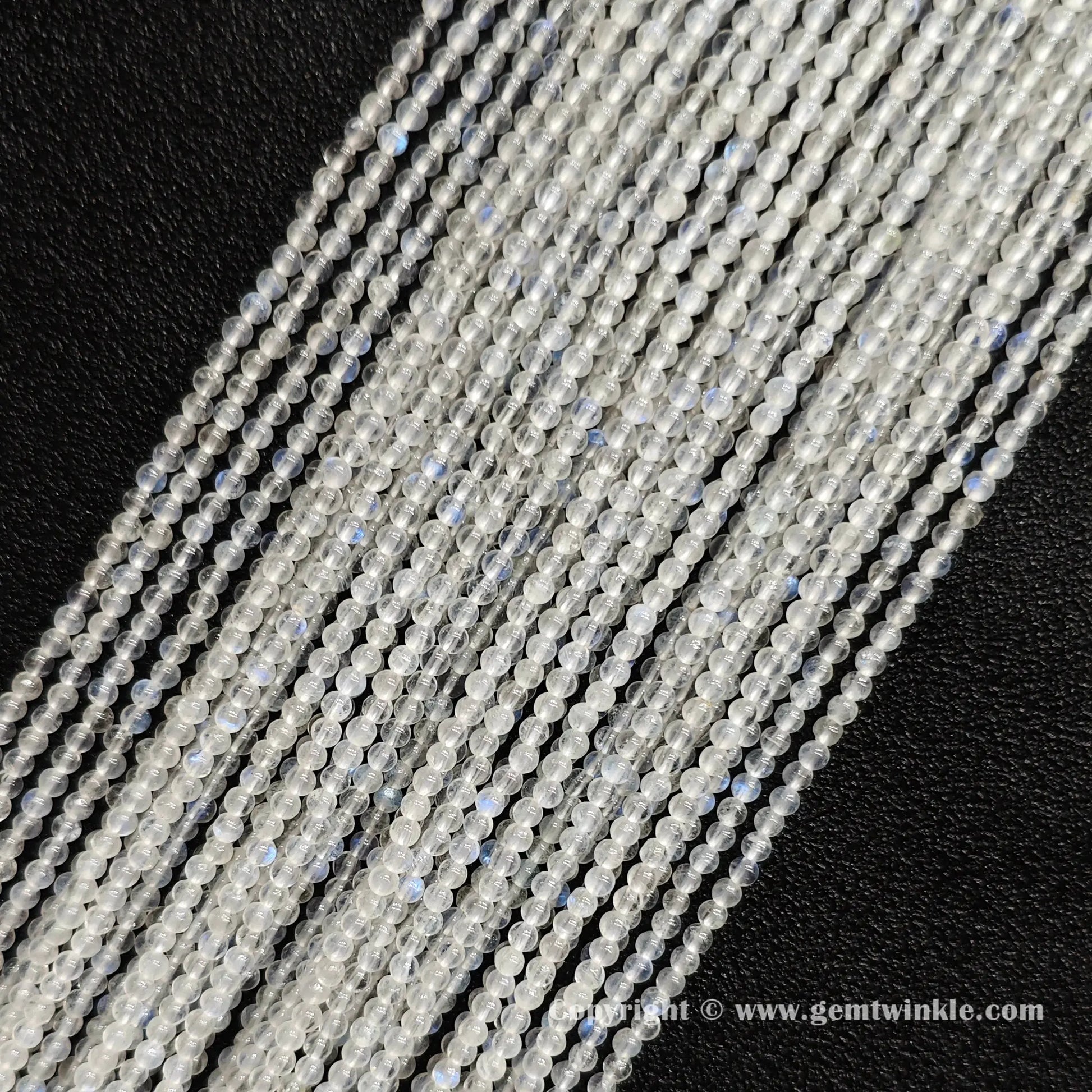 Angled view of 2mm micro blue flash moonstone seed bead strands laid parallel on dark textured surface