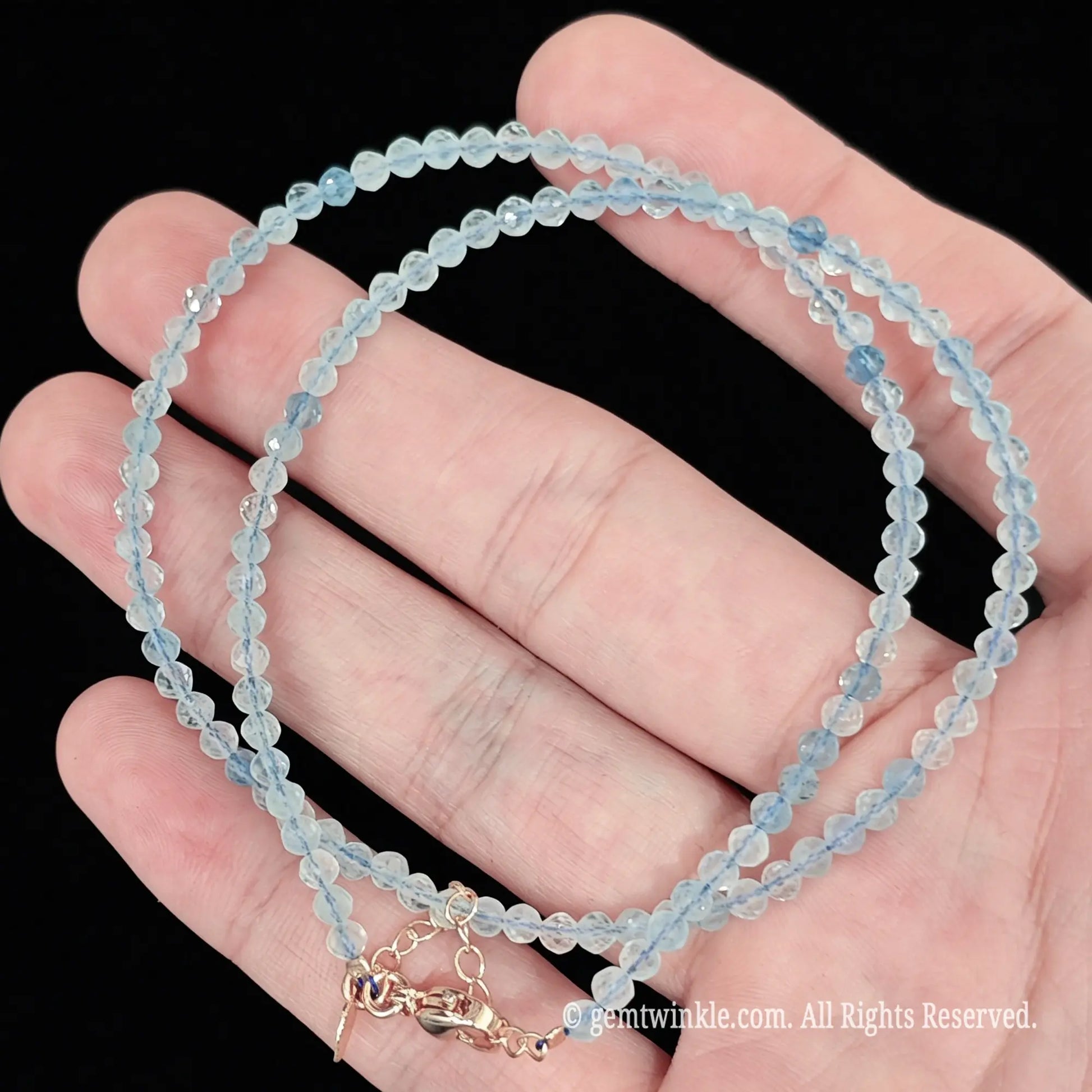 close up view of gold tone lobster clasp, extender chain and charm tag on aquamarine necklace