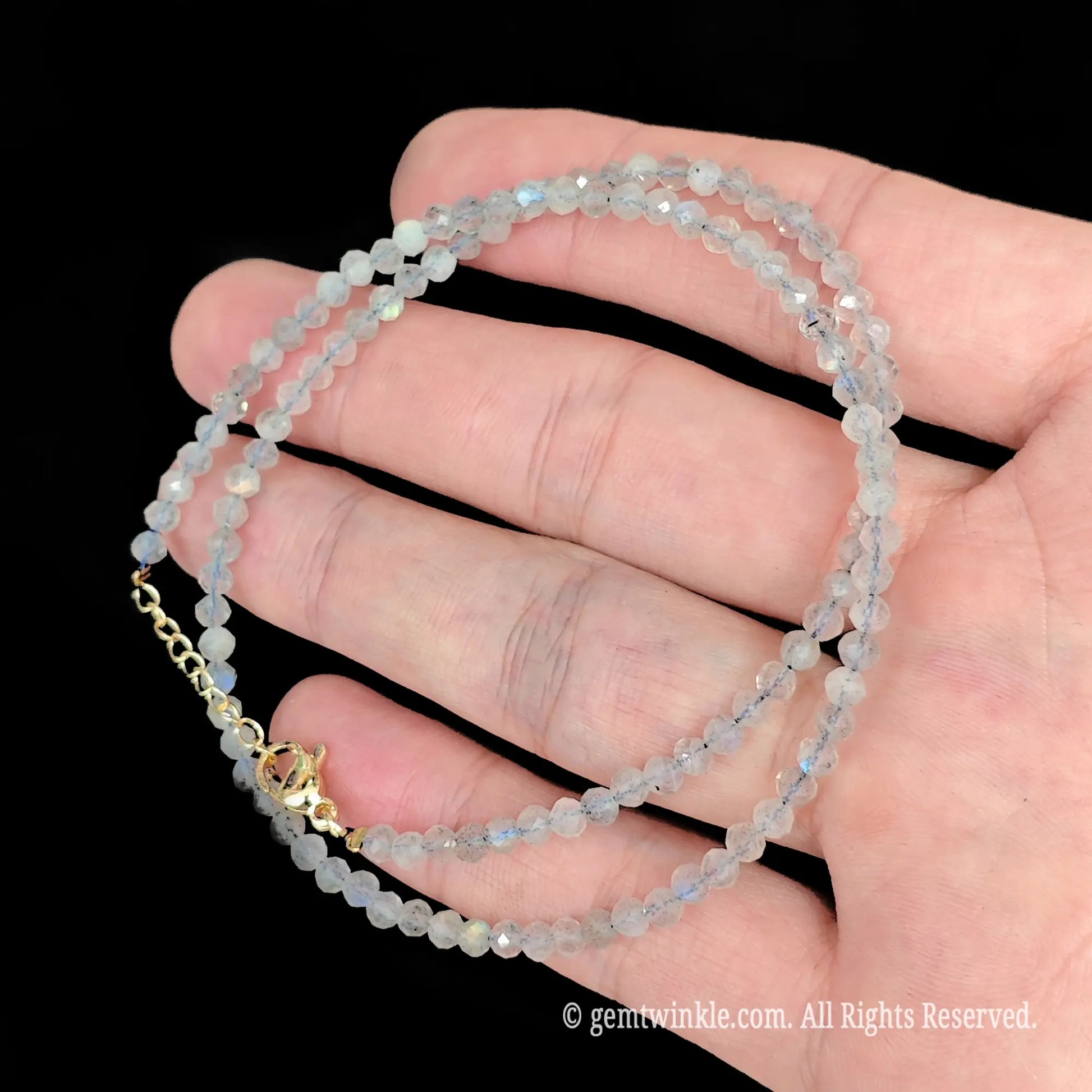 close up view of gold tone lobster clasp, extender chain and heart tag on grey moonstone necklace
