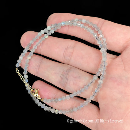 close up view of gold tone lobster clasp, extender chain and heart tag on grey moonstone necklace