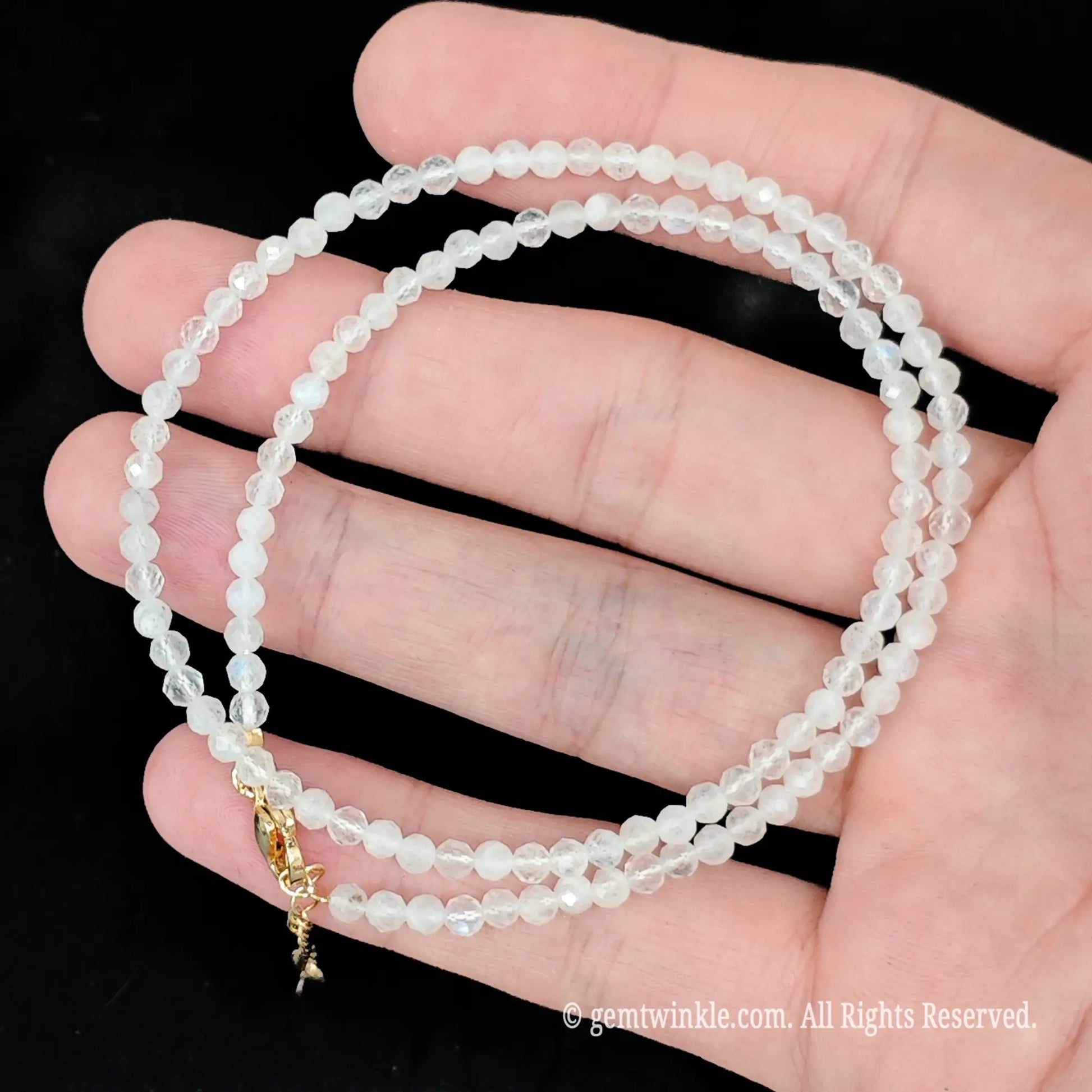 close up of gold tone lobster clasp and extension chain on white moonstone necklace