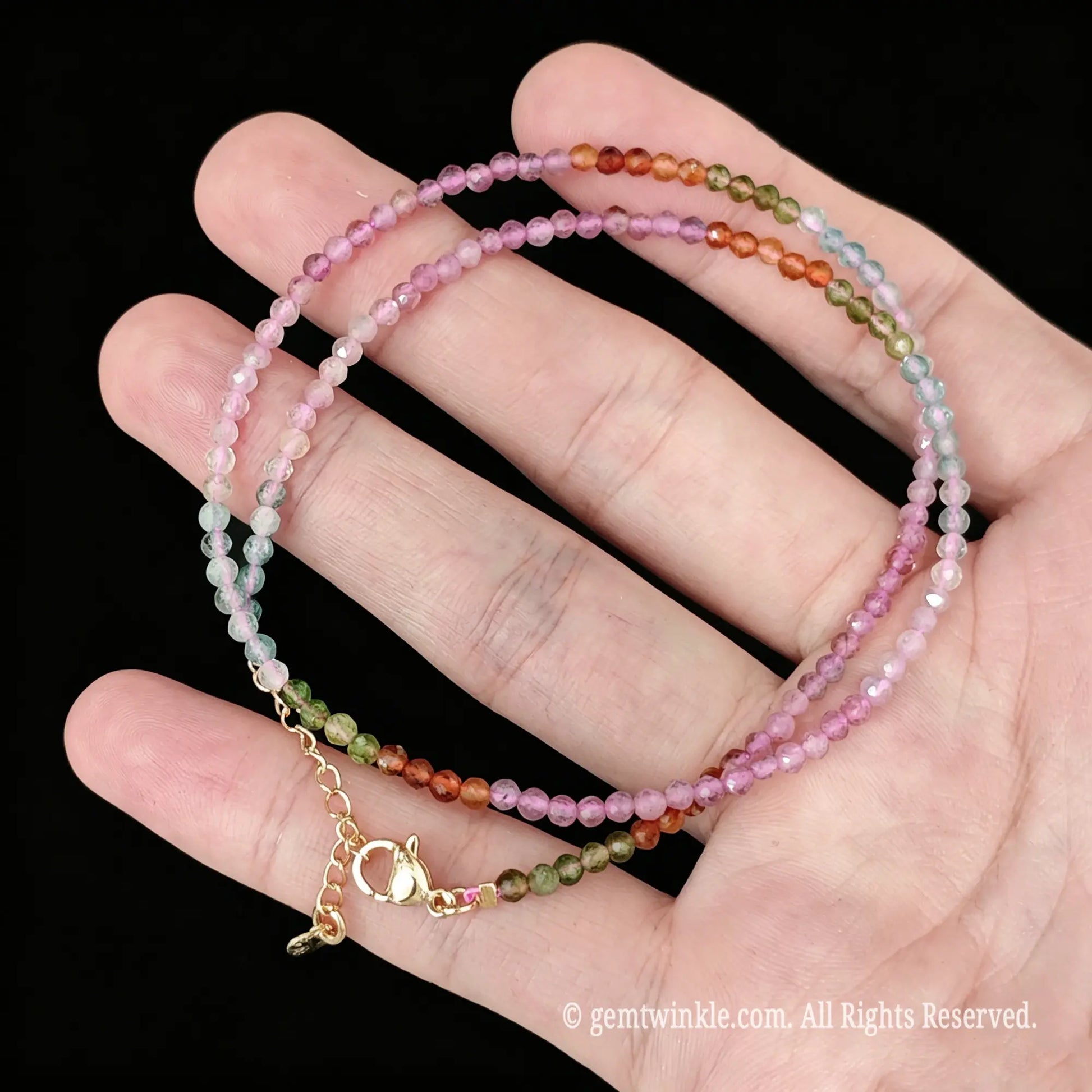 close up view of gold tone lobster clasp, extender chain and charm tag on multicolor tourmaline necklace