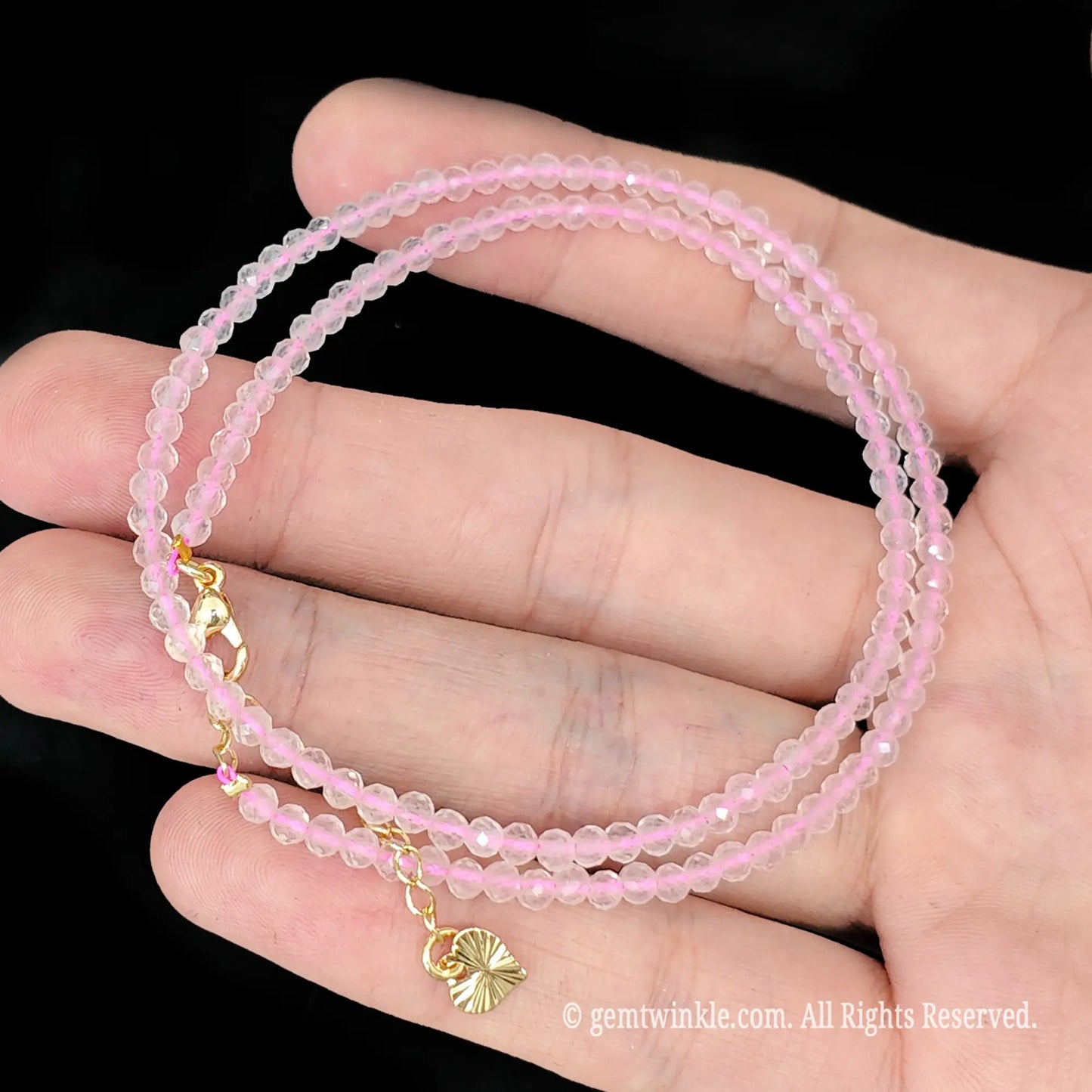 close up view of gold tone lobster clasp, extender chain and butterfly charm tag on rose quartz necklace