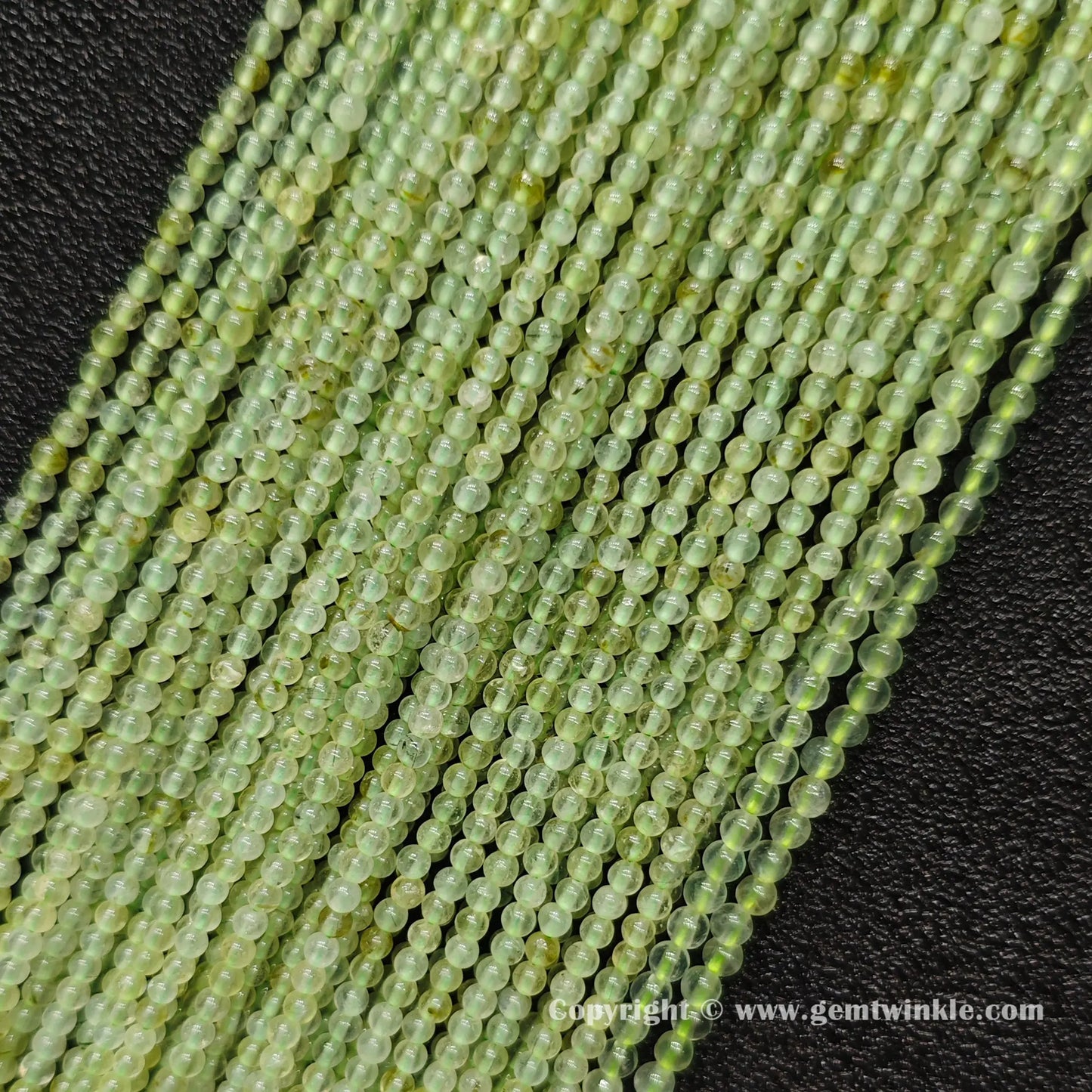 Angled view of clean 3mm prehnite round seed bead strands laid parallel on dark surface