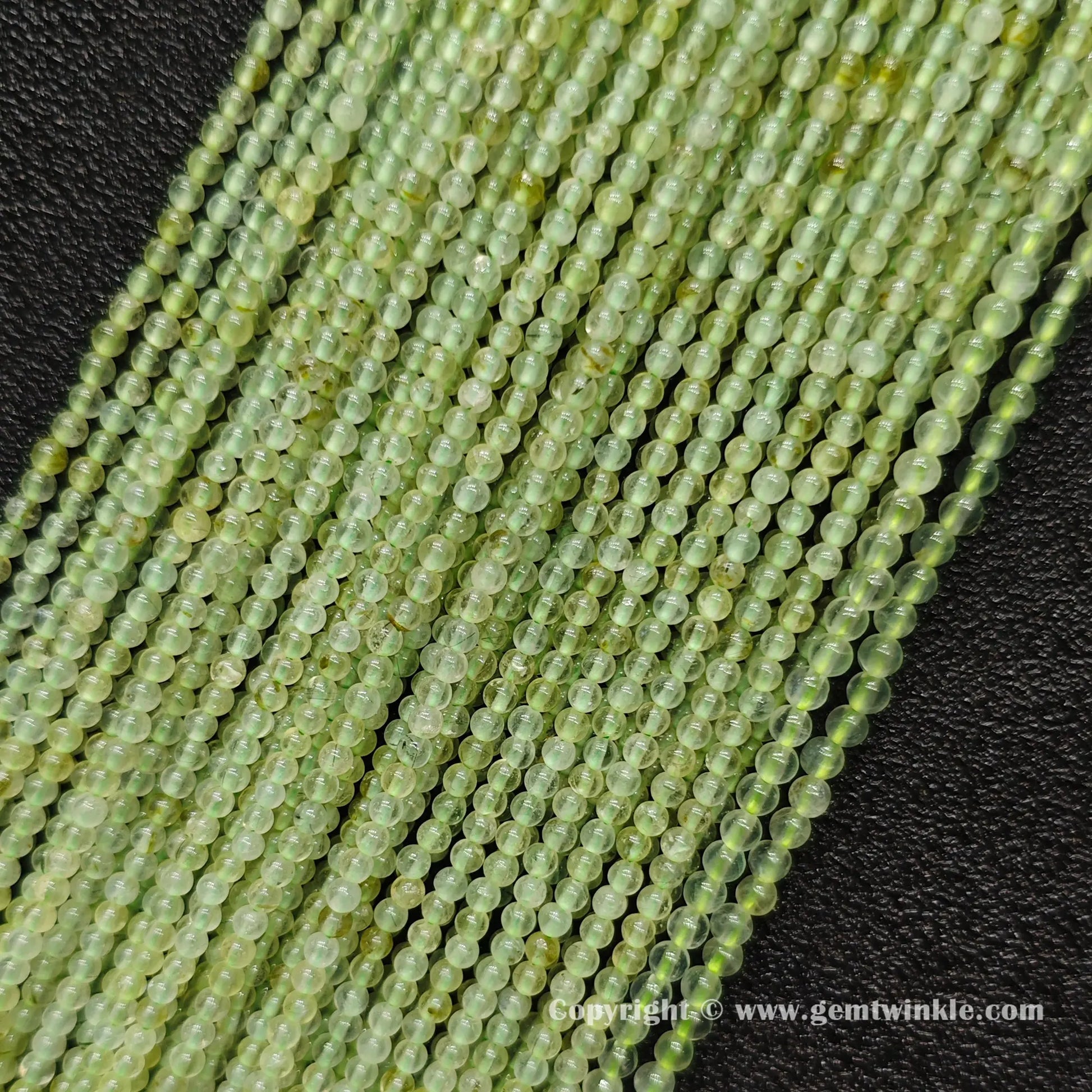 Angled view of clean 3mm prehnite round seed bead strands laid parallel on dark surface