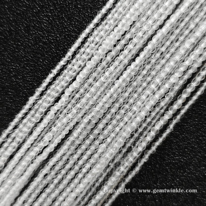 Angled view of 2mm and 3mm micro rock crystal round bead strands laid parallel on dark surface