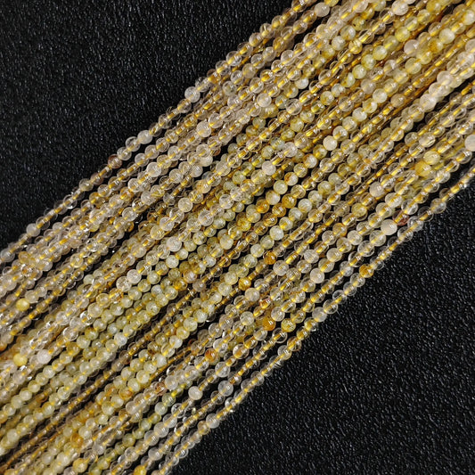Close up of 2mm micro seed beads showing tiny natural gold rutilated quartz strands with dense ice cracks on a dark surface