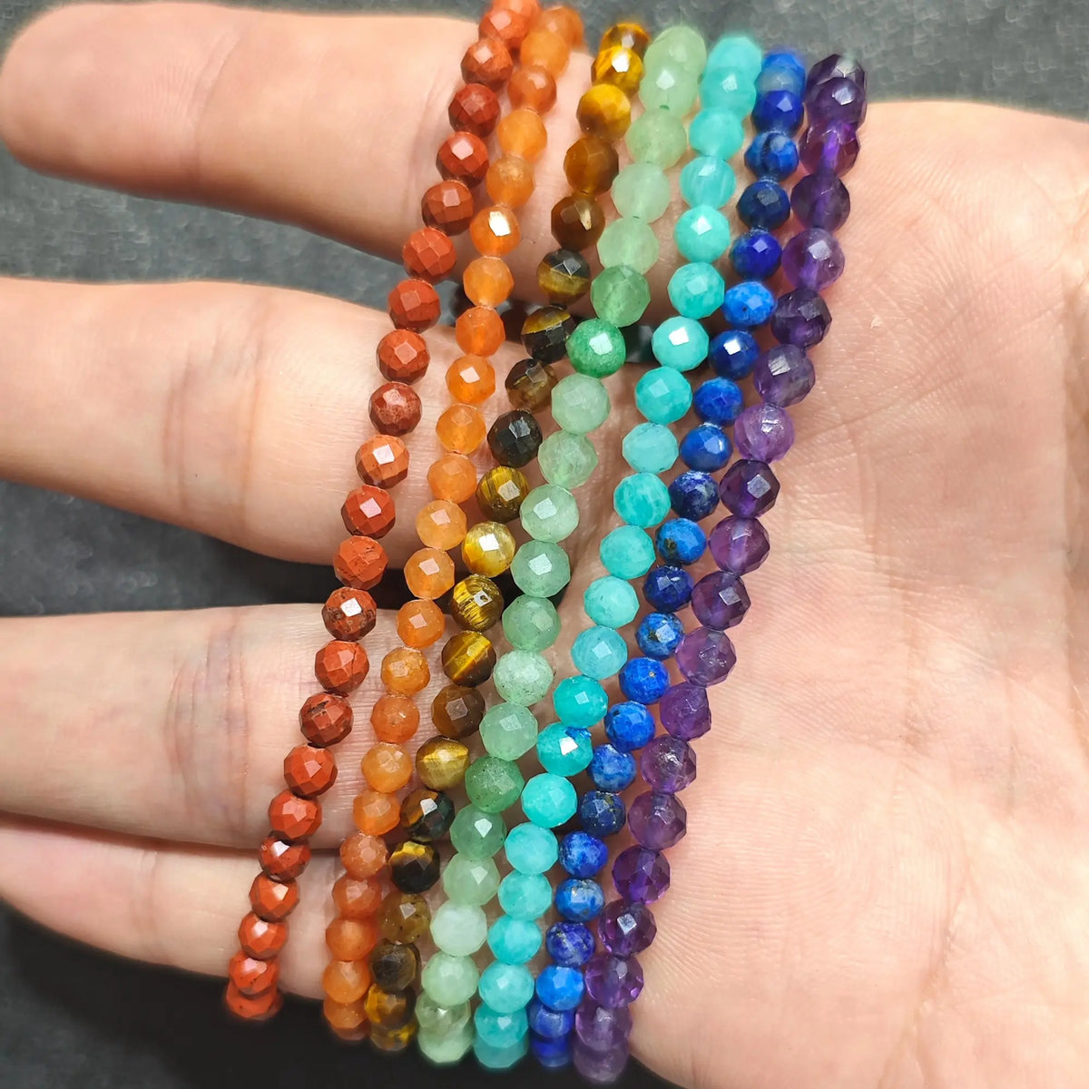 close up of 7 micro faceted natural gemstone stretch bracelets stacked together inside palm showing delicate bead cuts