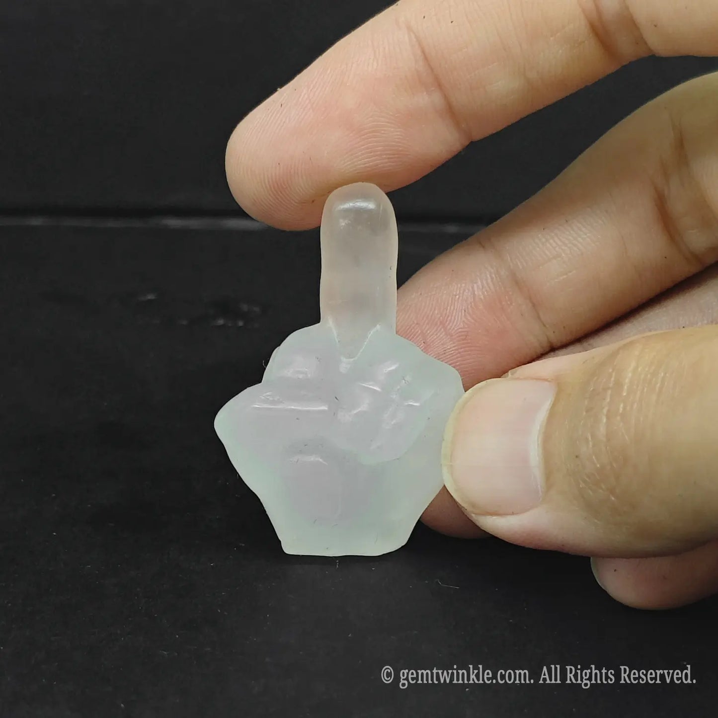 Handheld view of a milky white quartz middle finger carving showing rich cloud-like natural inclusions