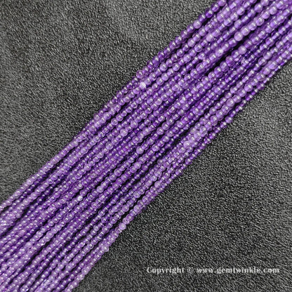Angled view of 2mm mini amethyst gemstone strands laid parallel on dark textured surface