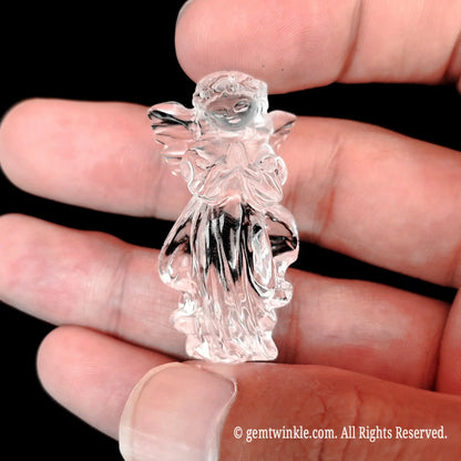 Hand holding a 4cm carved clear quartz guardian angel figurine across open palm for scale reference