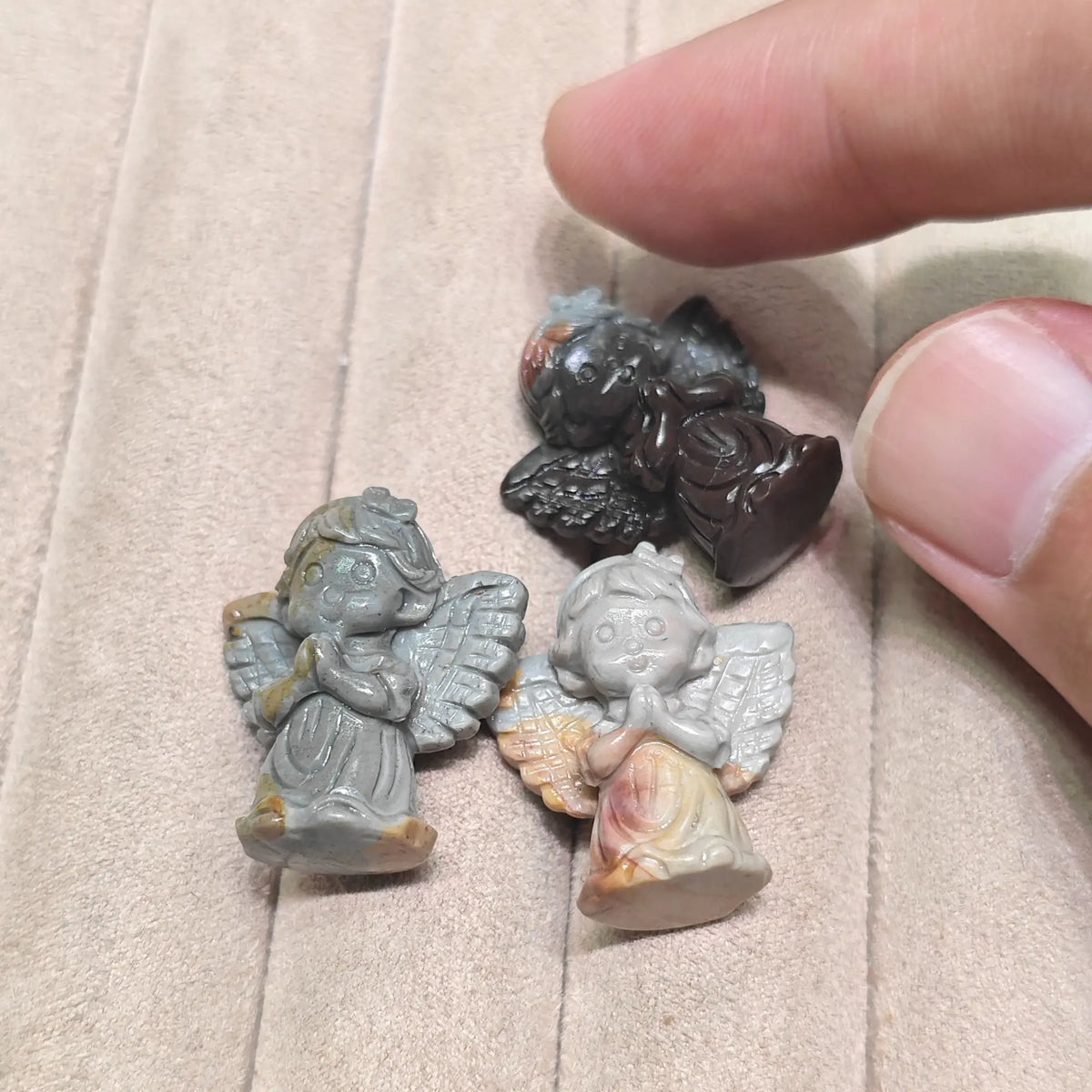 A group assortment of small carved stone angel figurines displayed together on a soft tray surface