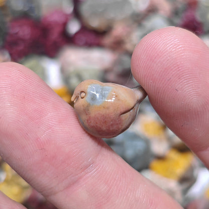 Fingertip holding a micro miniature fat bird sculpture displaying slate blue and tan color zoning