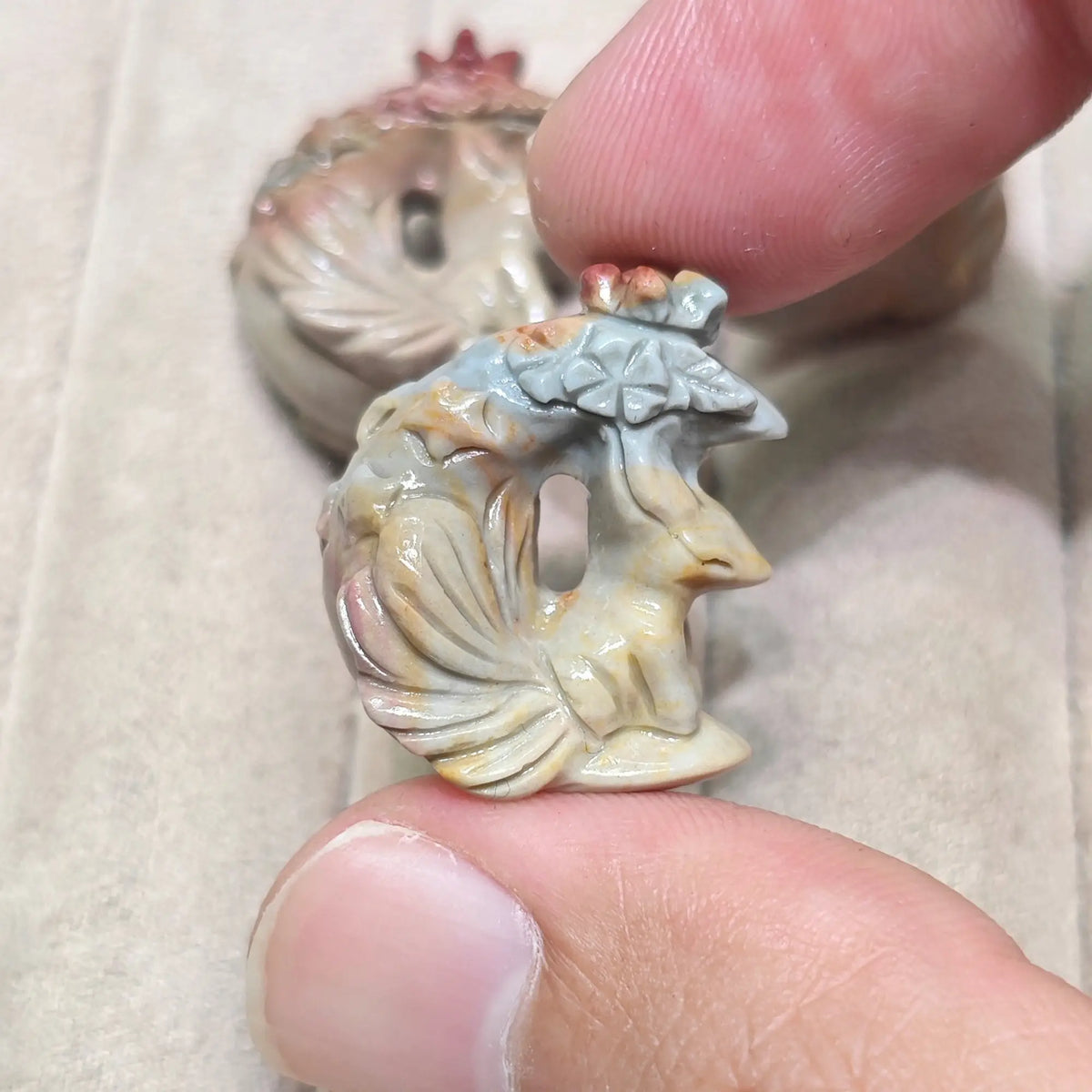 Hand holding a miniature moon fox figurine against a soft jewelry display tray background showing subtle color variations