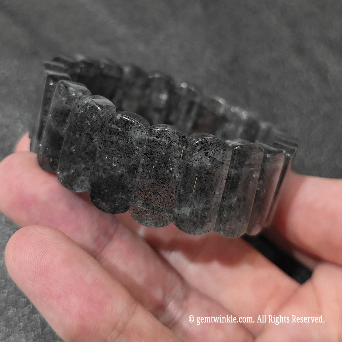 Side angle view of a minimalist biotite quartz rectangle stretch wristlet showing natural black flecks inside clear quartz