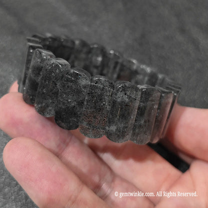 Side angle view of a minimalist biotite quartz rectangle stretch wristlet showing natural black flecks inside clear quartz