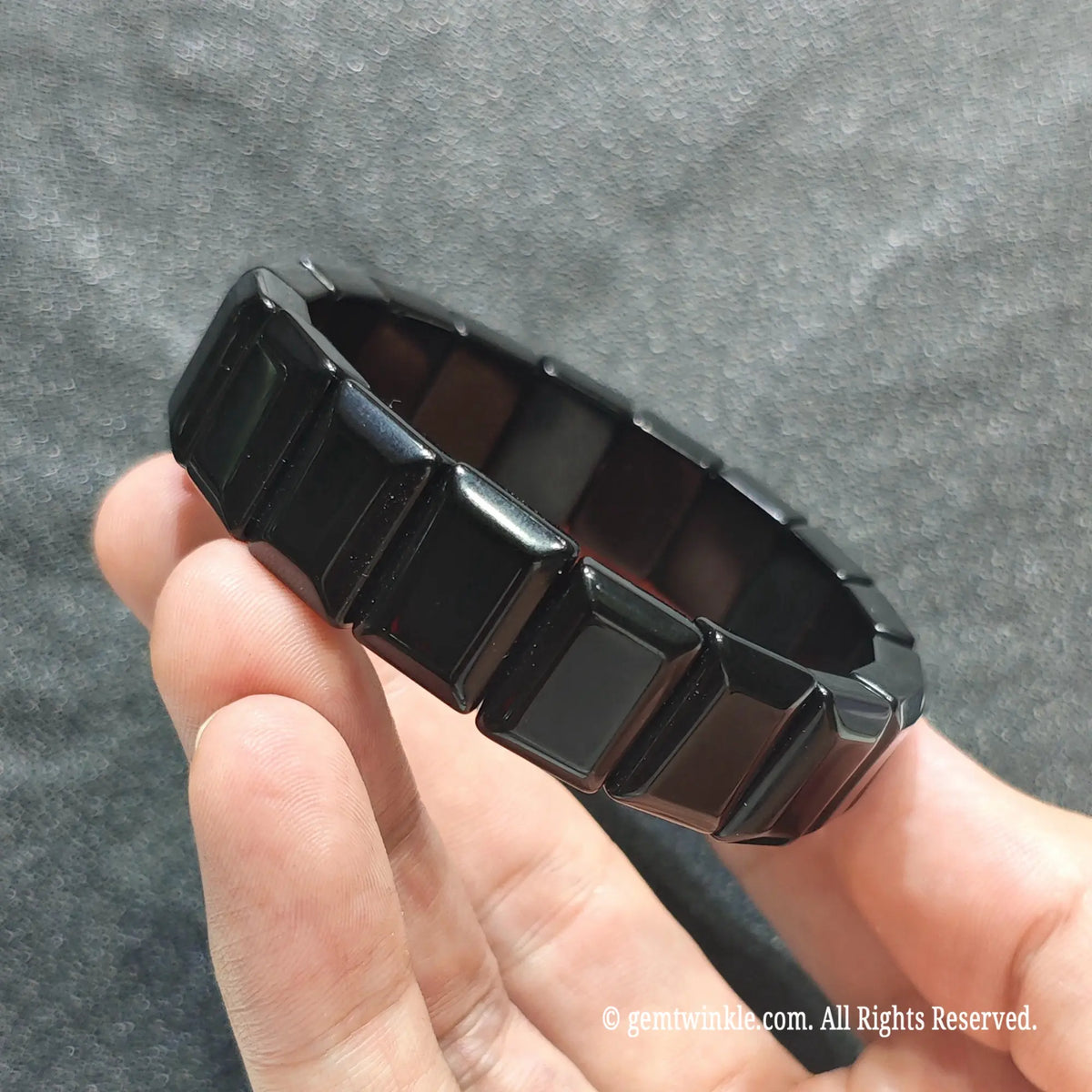 Full view of a minimalist black obsidian gemstone strand held in hand showing smooth reflective luster
