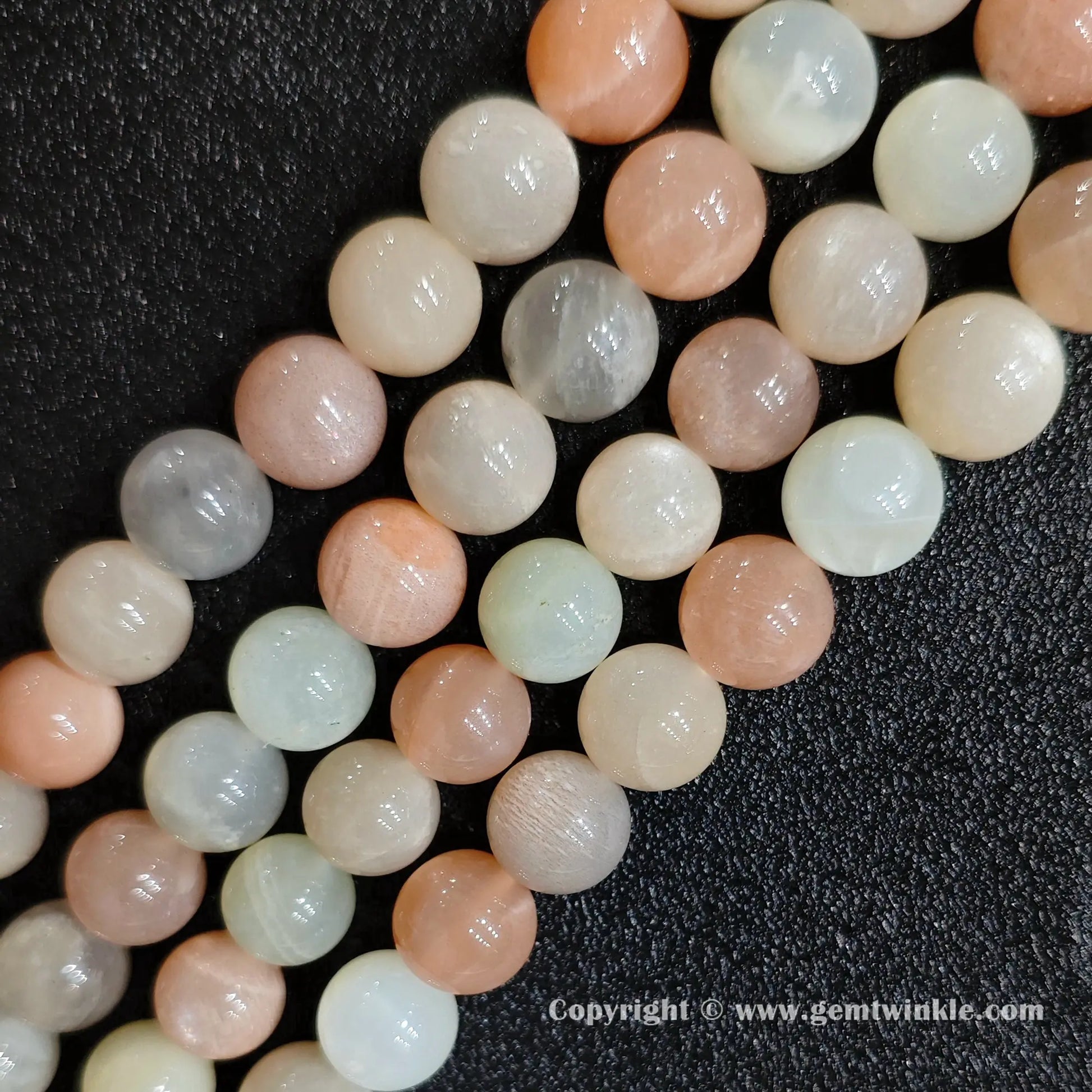 Angled view of natural peach feldspar moonstone sunstone strands arranged parallel on dark background