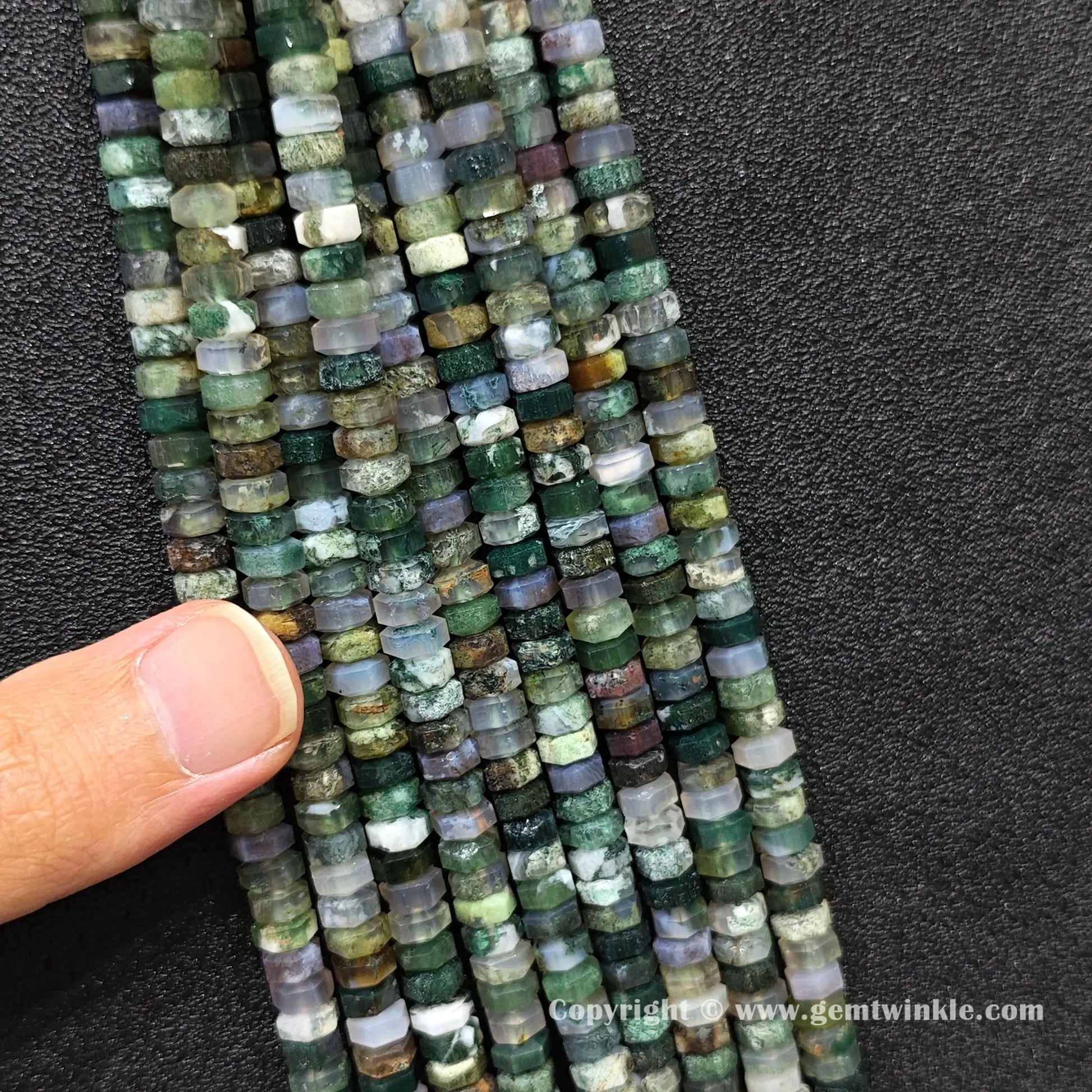 Close up view of 6x3mm moss agate faceted disc rondelle beads inspected on fingers for quality preview