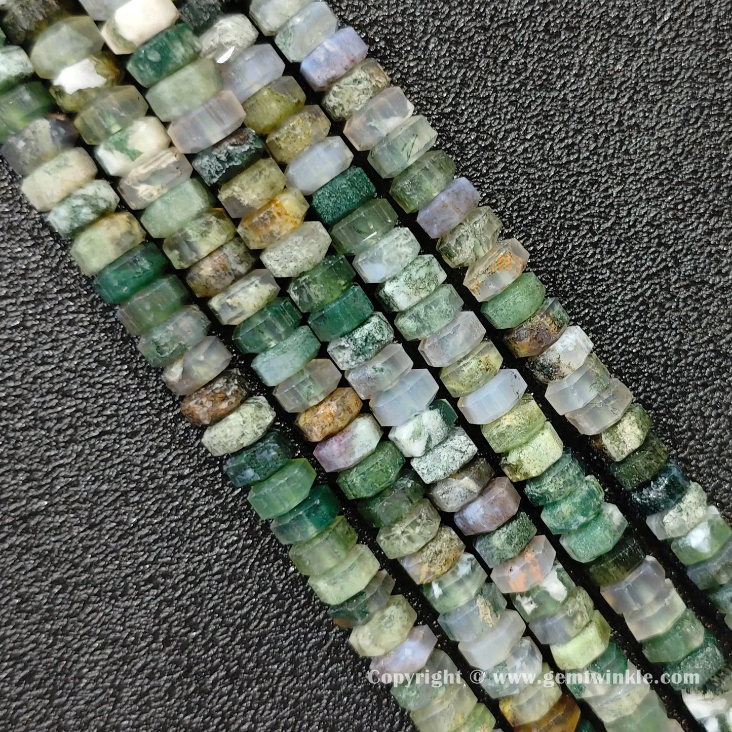 Angled view of natural moss agate faceted disc gemstone strands arranged parallel on dark background