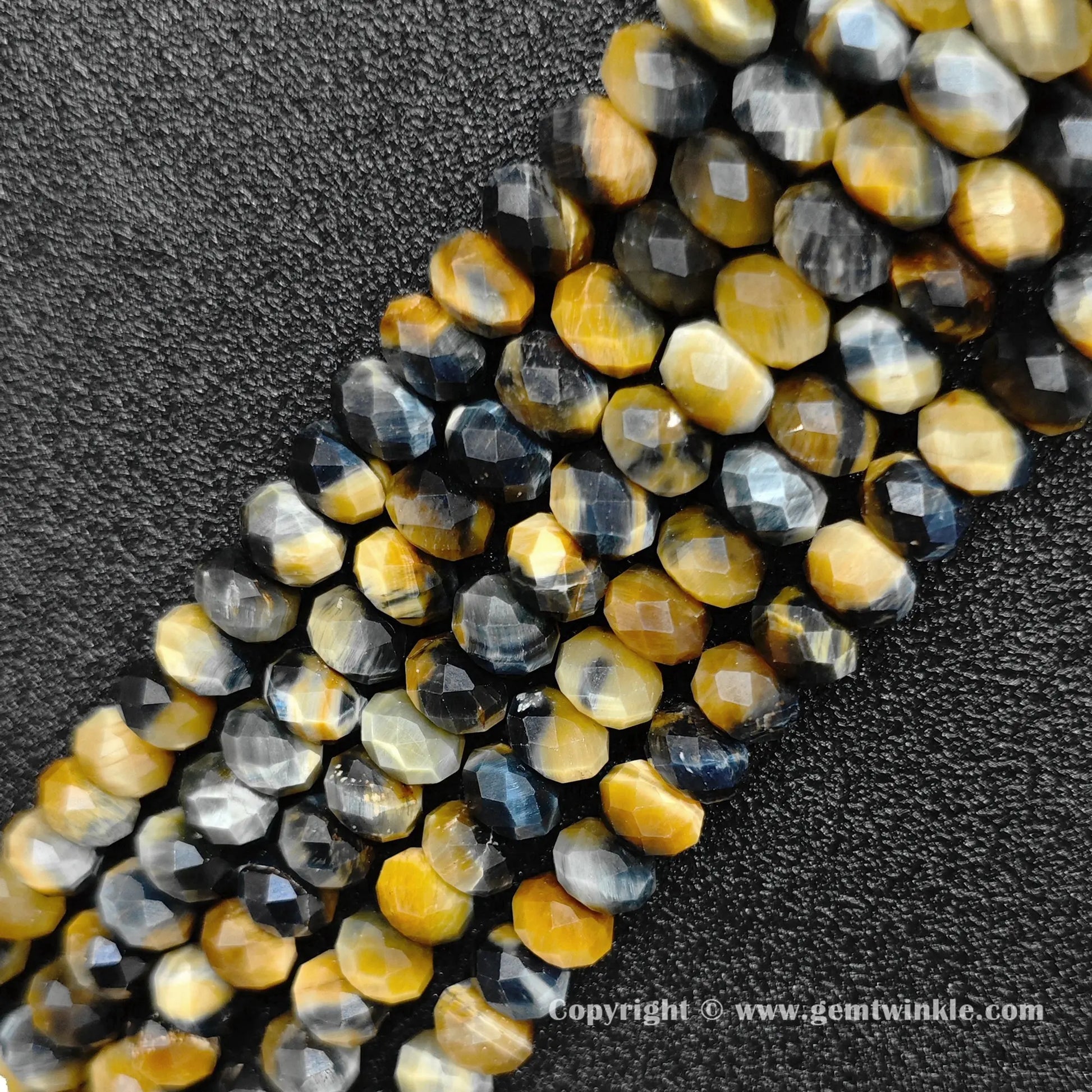 Angled view of multi color tiger eye faceted disc bead strands laid parallel on dark surface