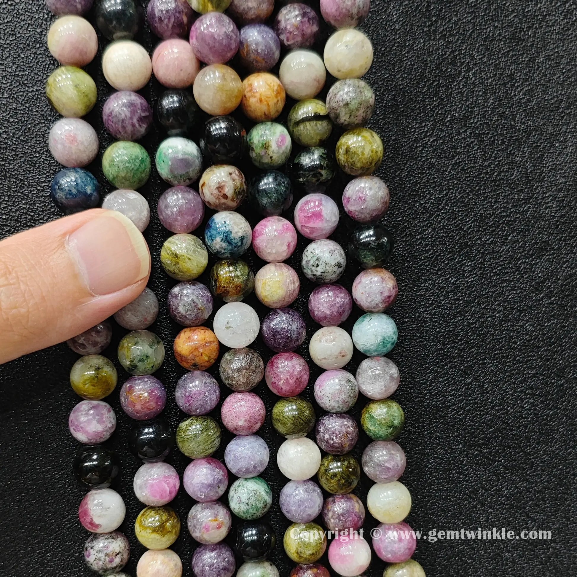 Finger holding natural multi color tourmaline bead strands demonstrating scale for jewelry makers