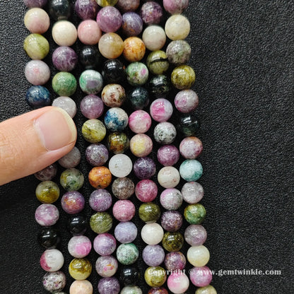 Finger holding natural multi color tourmaline bead strands demonstrating scale for jewelry makers