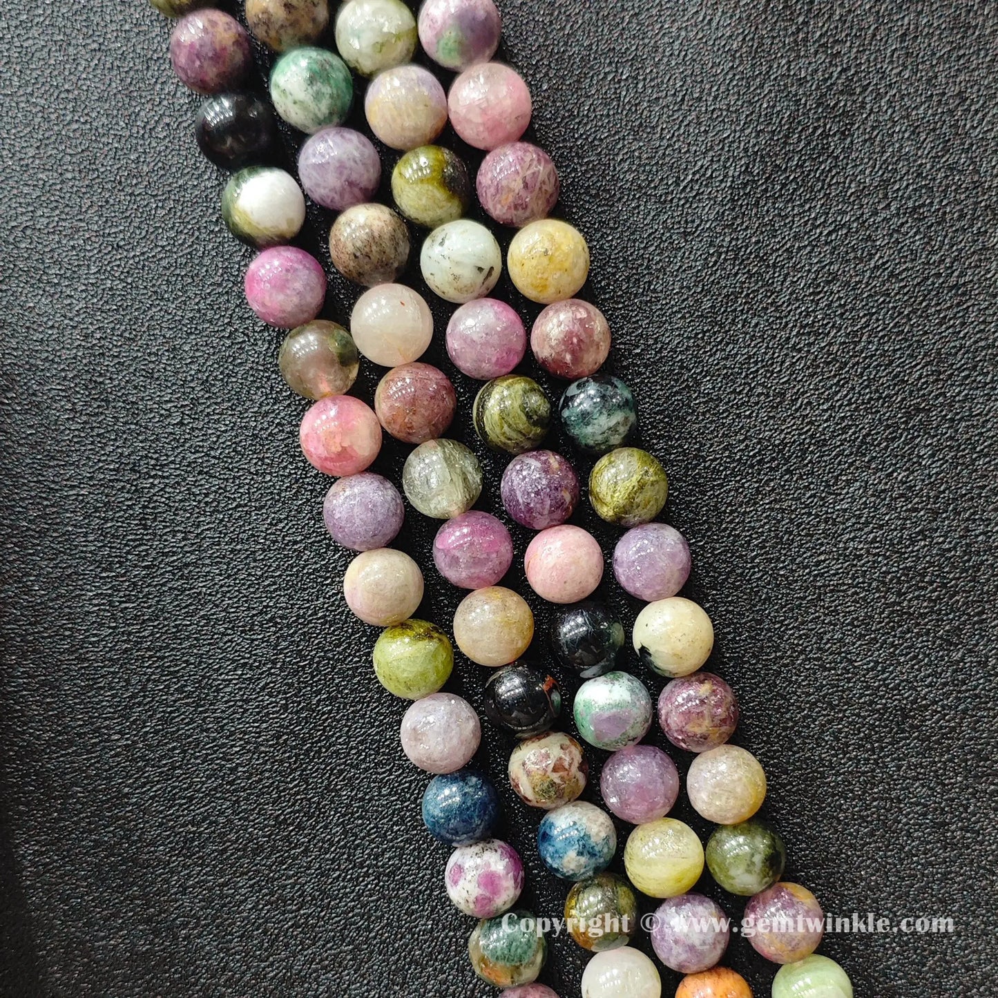 Multiple strands of natural multi color tourmaline round beads lined up on dark surface
