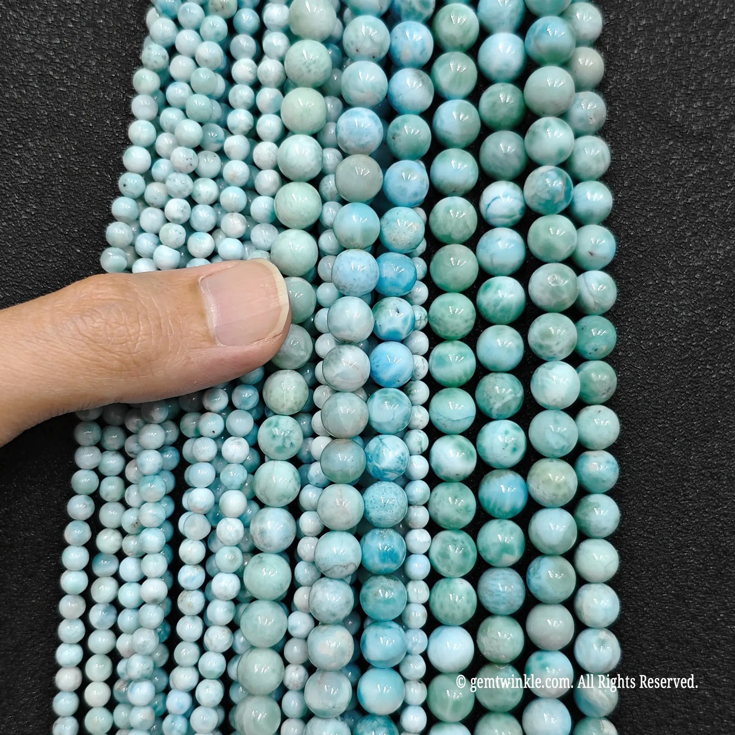 Multi size grid larimar tiny crystal round beads with a hand inspecting the three to eight millimeter strands
