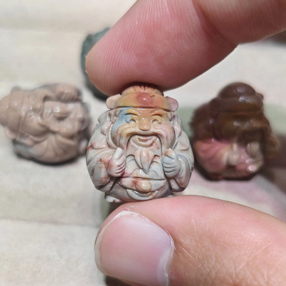 multi color carved caishen god of wealth statue held in fingers with other colored figurines resting in background