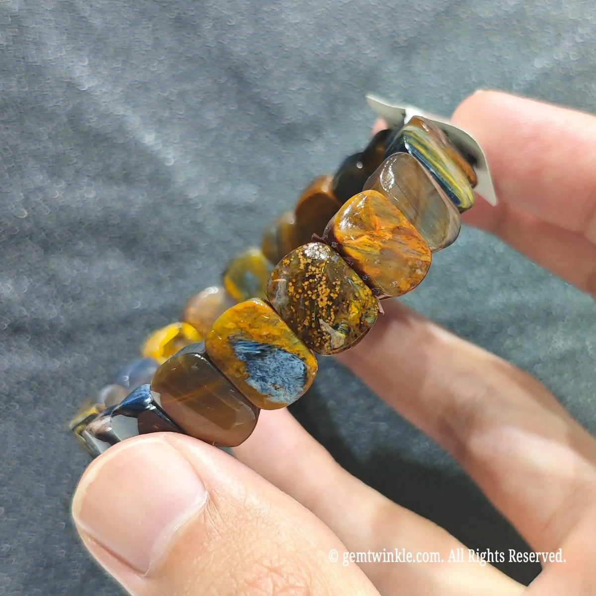 Close up view of multicolor pietersite plate beads showing smooth polish and chaotic gold and blue fibers[cite: 6]