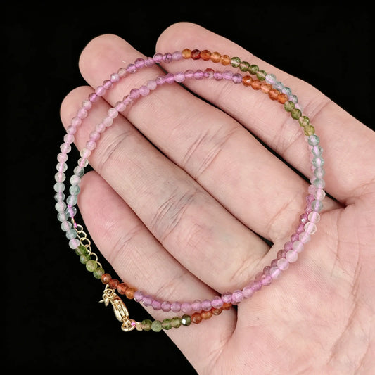 multicolor tourmaline micro faceted bead strand held in hand with gold clasp