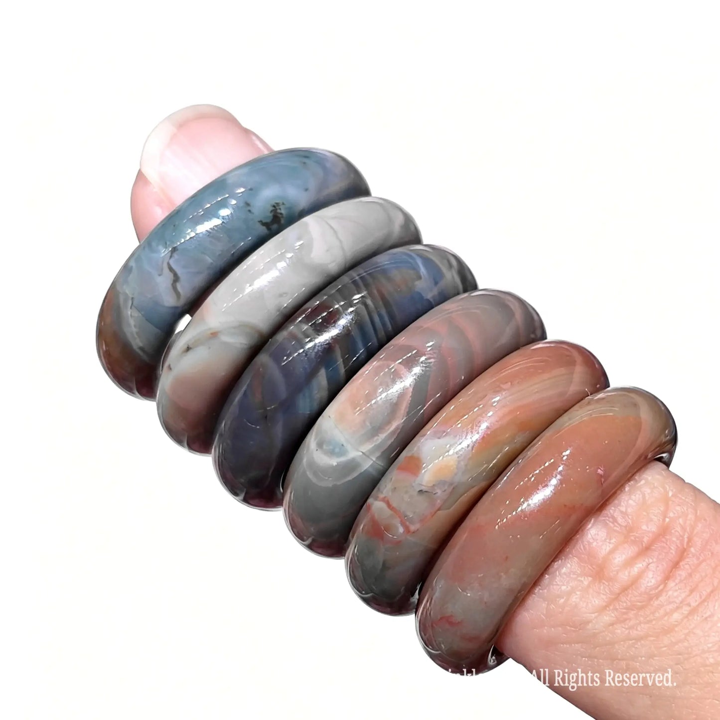 Stack of multicolor Alashan Gobi agate gemstone rings on finger showing 16mm to 22mm inner diameter sizes and natural textures