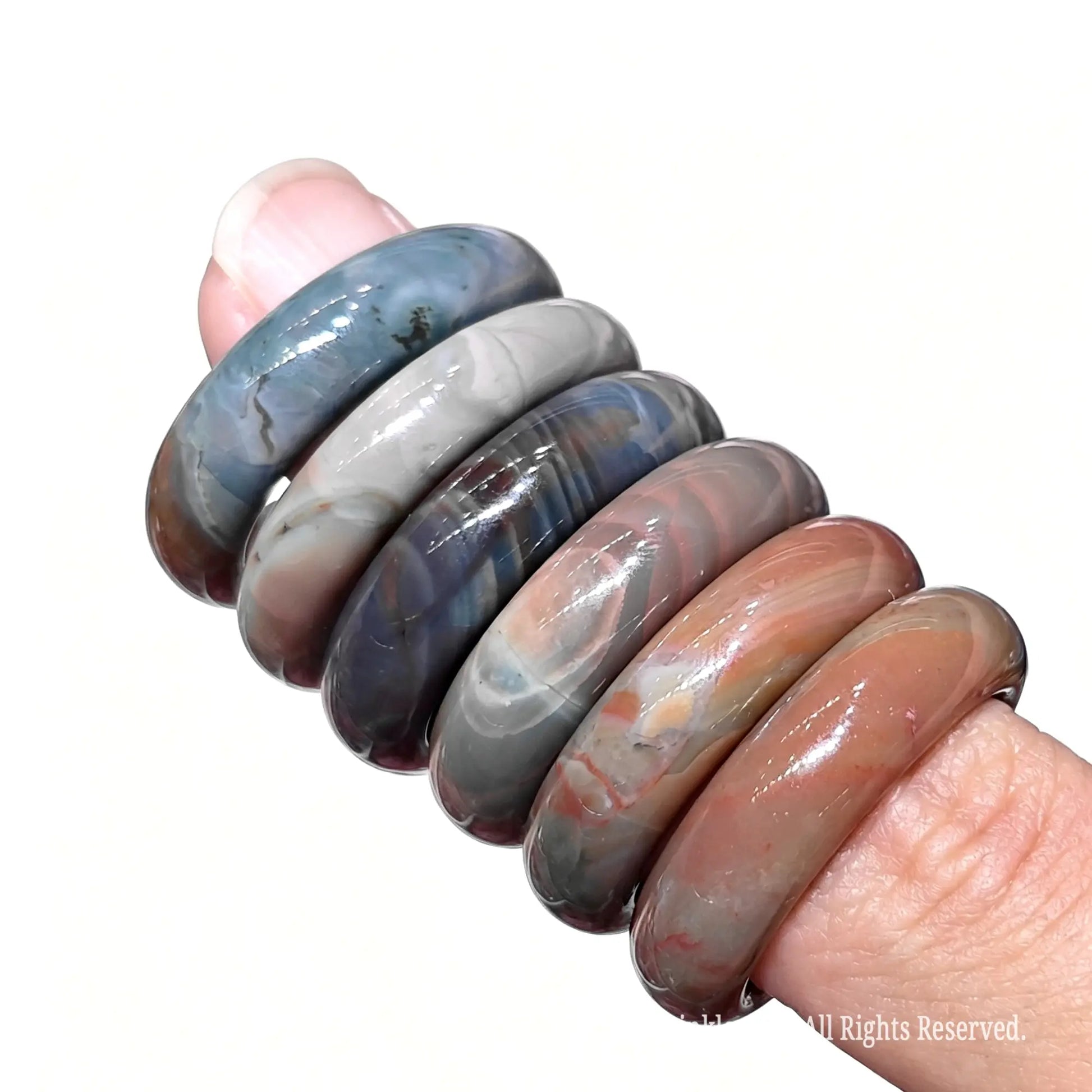 Stack of multicolor Alashan Gobi agate gemstone rings on finger showing 16mm to 22mm inner diameter sizes and natural textures