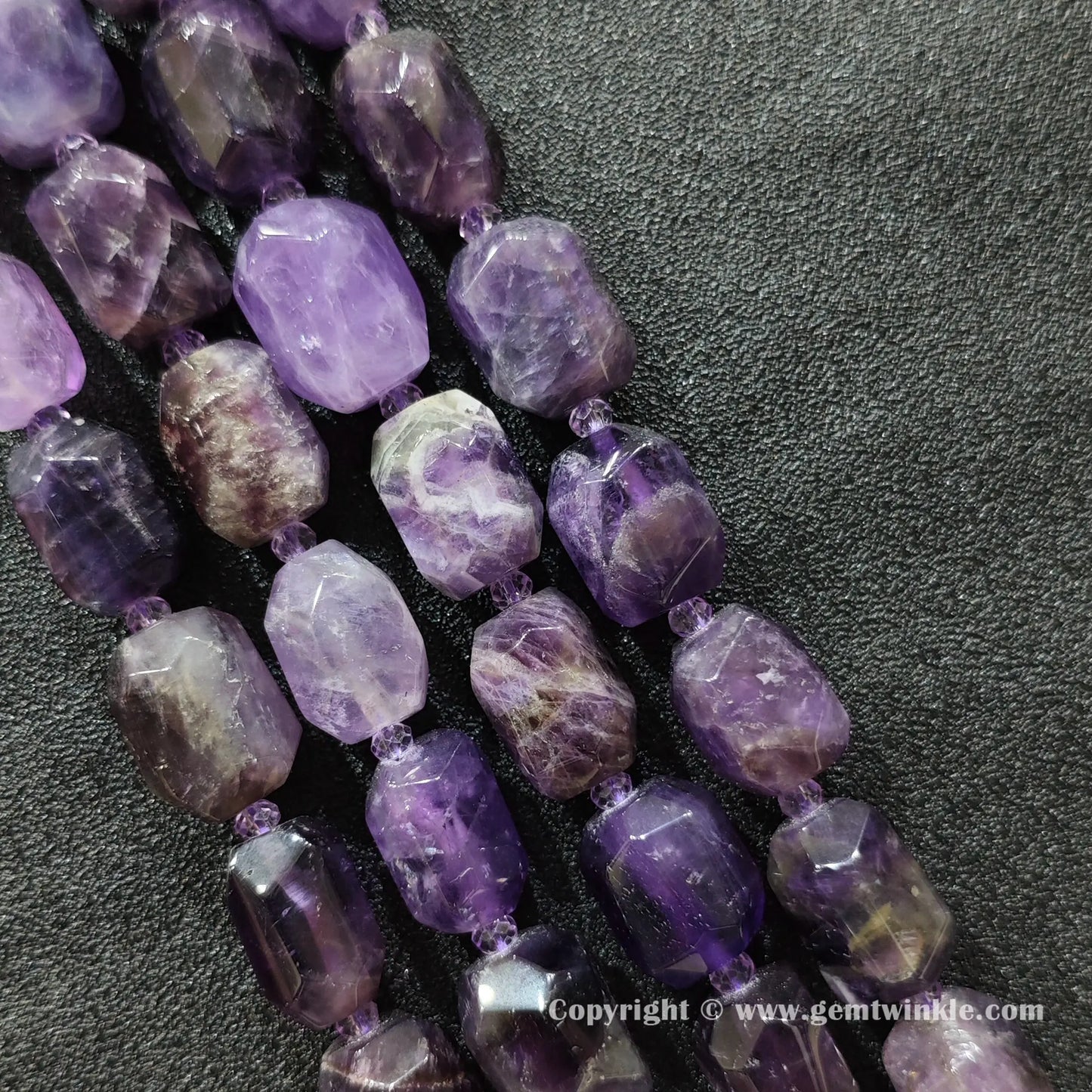 multiple strands of chunky amethyst faceted barrel beads on dark fabric surface