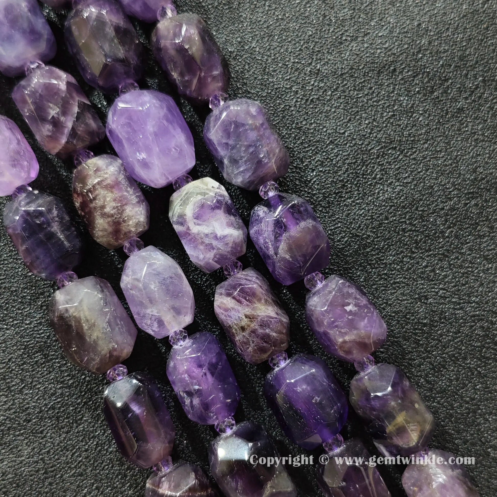 multiple strands of chunky amethyst faceted barrel beads on dark fabric surface