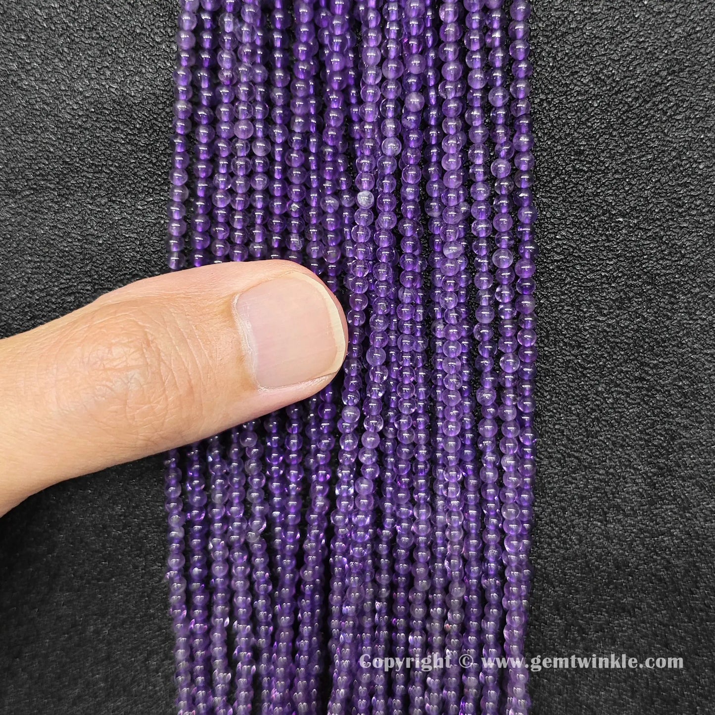 Close up view of natural 2mm amethyst round beads held on hand for live size and color inspection