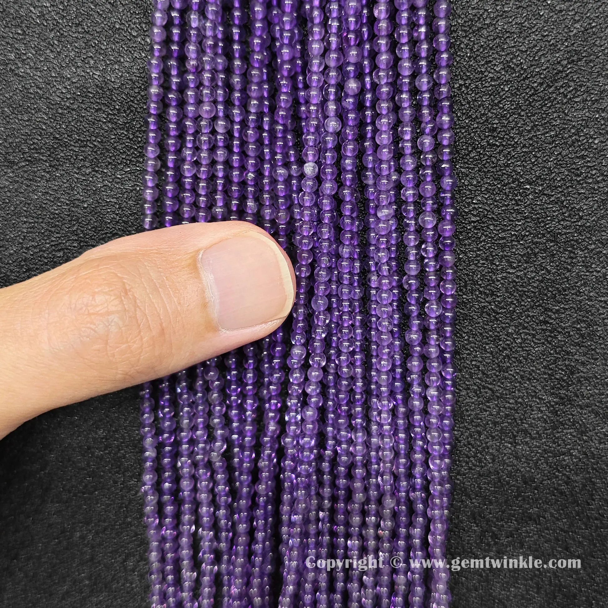 Close up view of natural 2mm amethyst round beads held on hand for live size and color inspection