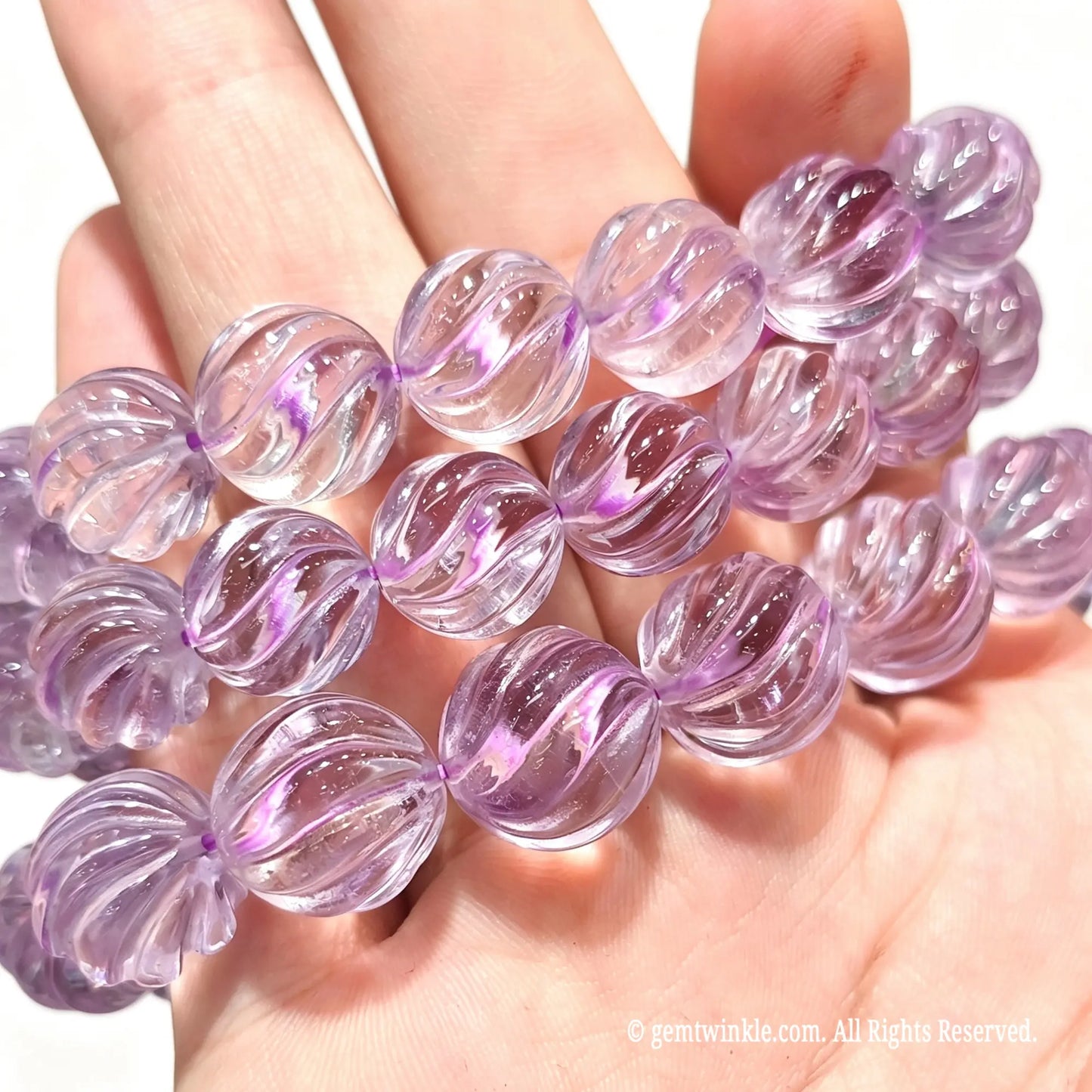 Palm view of three natural lavender amethyst carved pumpkin bead stretch bracelets displaying pale purple translucency