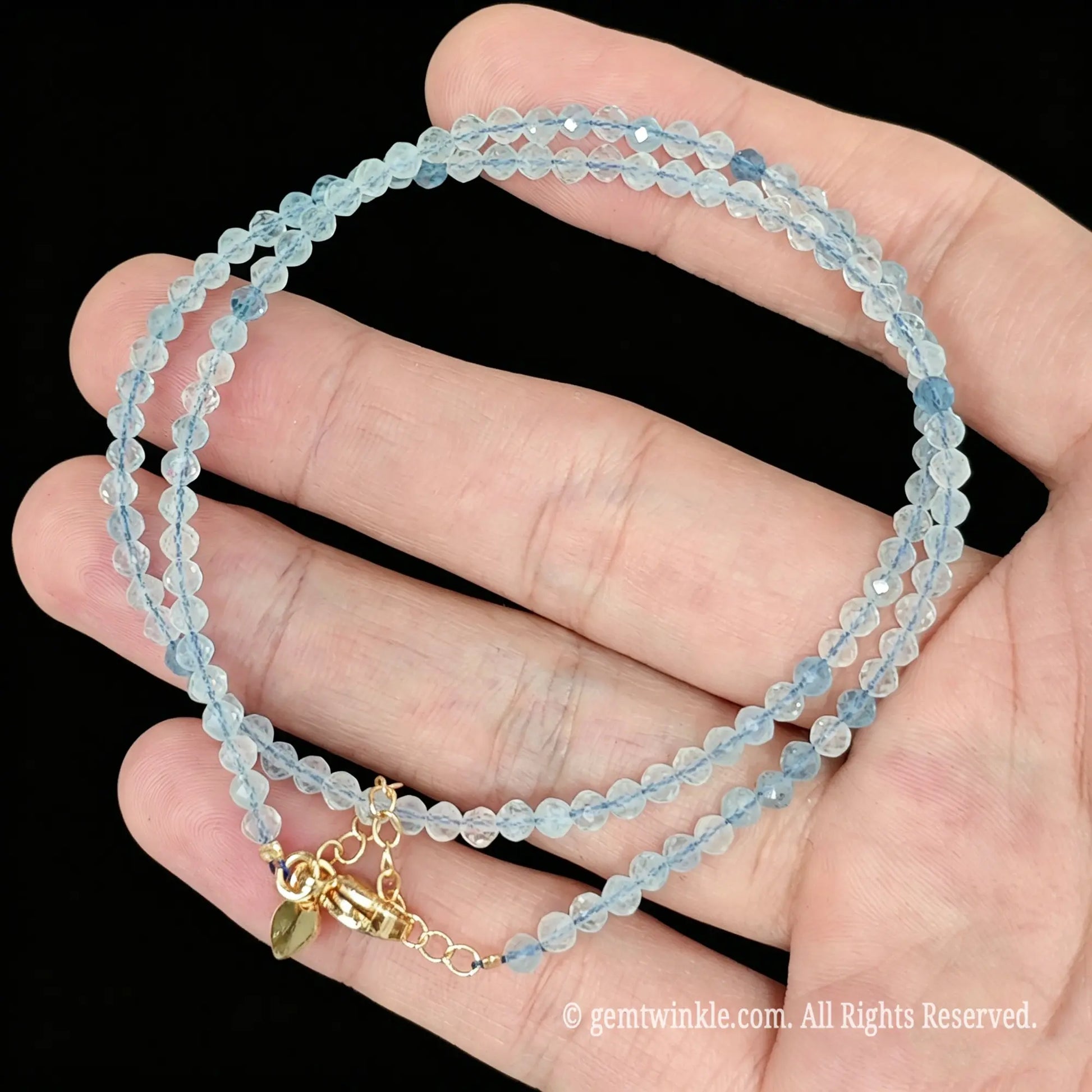 single strand aquamarine collar necklace coiled across palm showing icy blue translucency