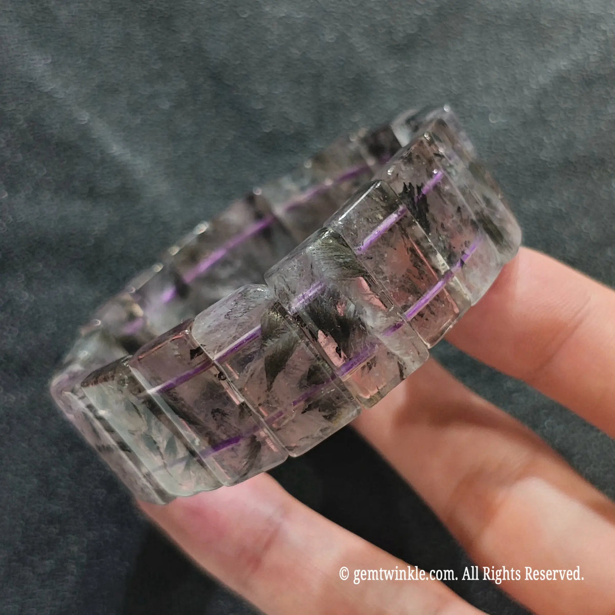 Hand holding a natural auralite 23 unisex boho bracelet featuring rectangle beads with purple amethyst and dark inclusions