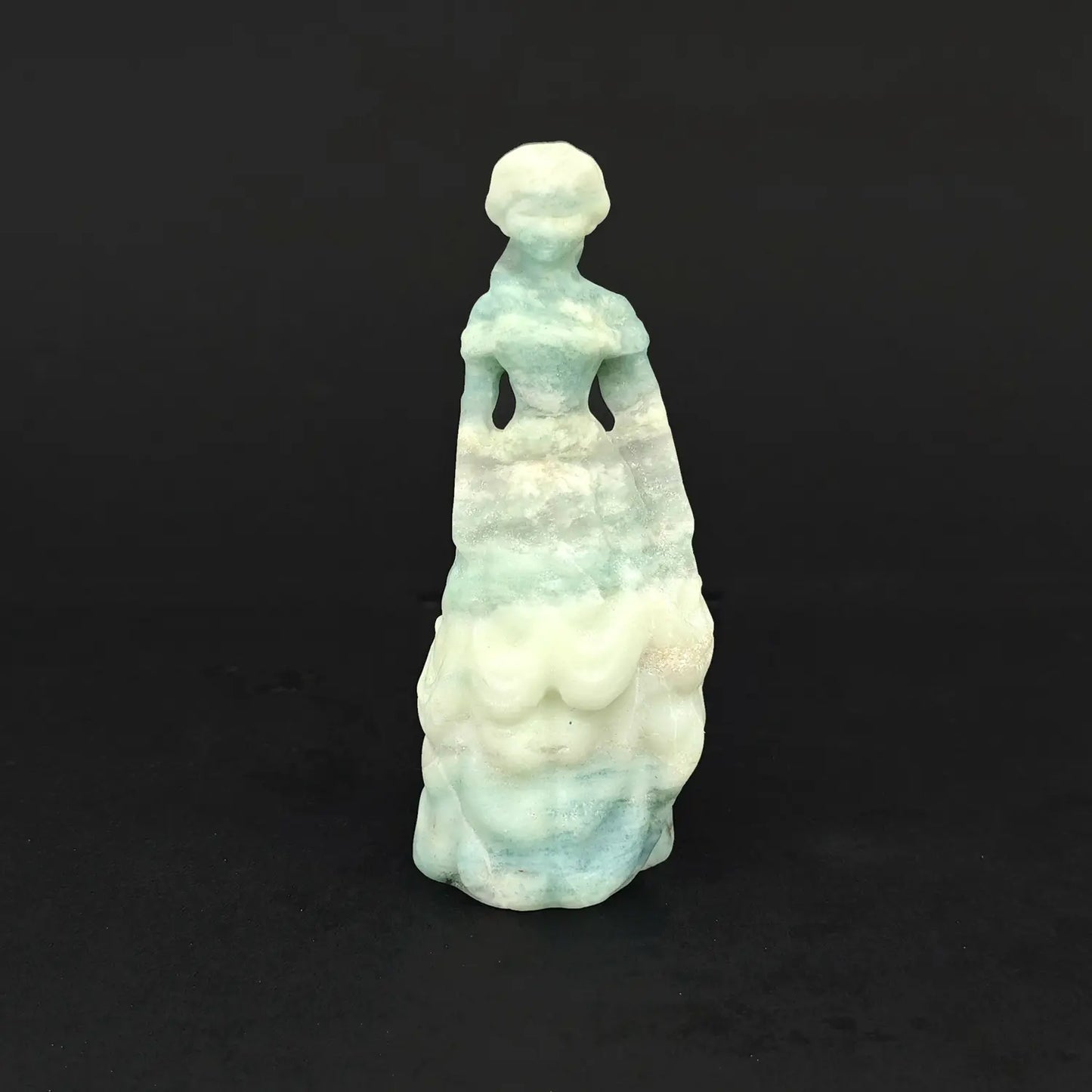 A 4-inch hand-carved natural ocean banded crystal princess statue in a mint green and white tiered ball gown on a dark background