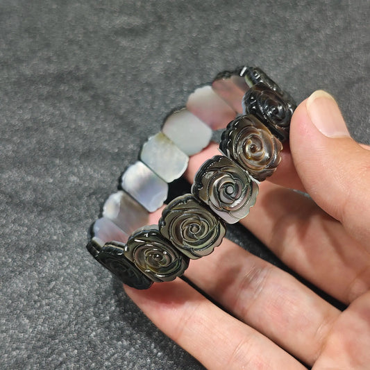 Natural black mother of pearl carved rose flower plate bead stretch bangle bracelet held in hand showing dark peacock shell sheen