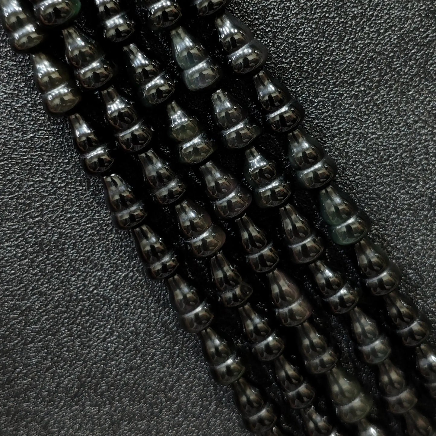 Macro closeup of natural black obsidian gourd beads showing smooth polish and calabash shape