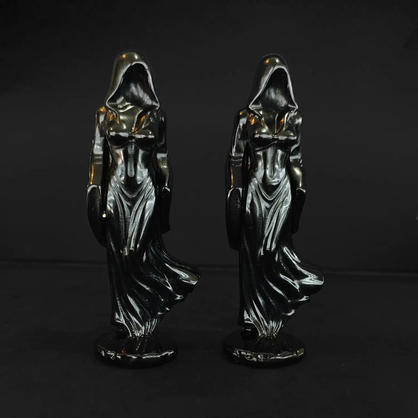 Two 10cm natural black obsidian shrouded goddess statues with flowing cloaks standing front facing against a dark background