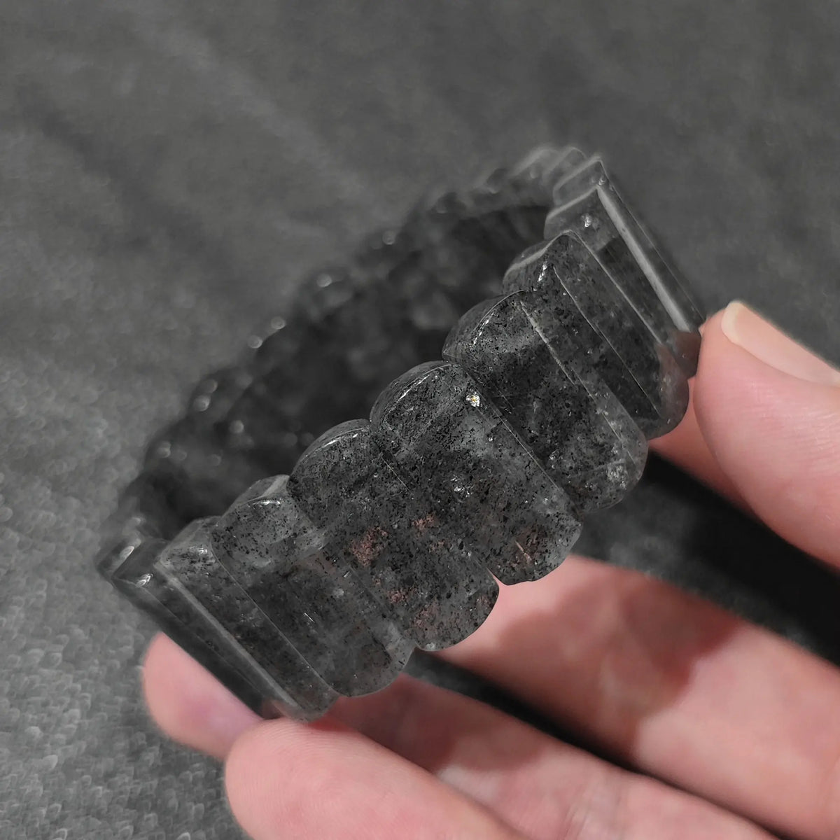 Hand holding a natural black strawberry quartz unisex boho bracelet with 20x9mm rectangle beads showing shimmering biotite mica