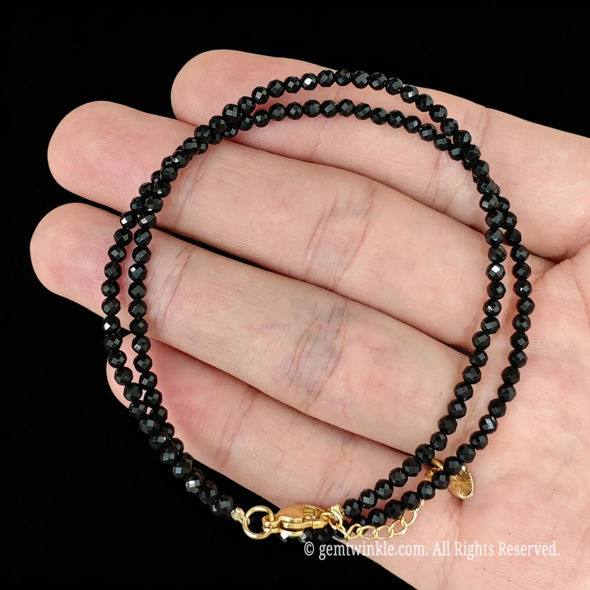 single strand black tourmaline collar necklace coiled across palm showing glassy luster