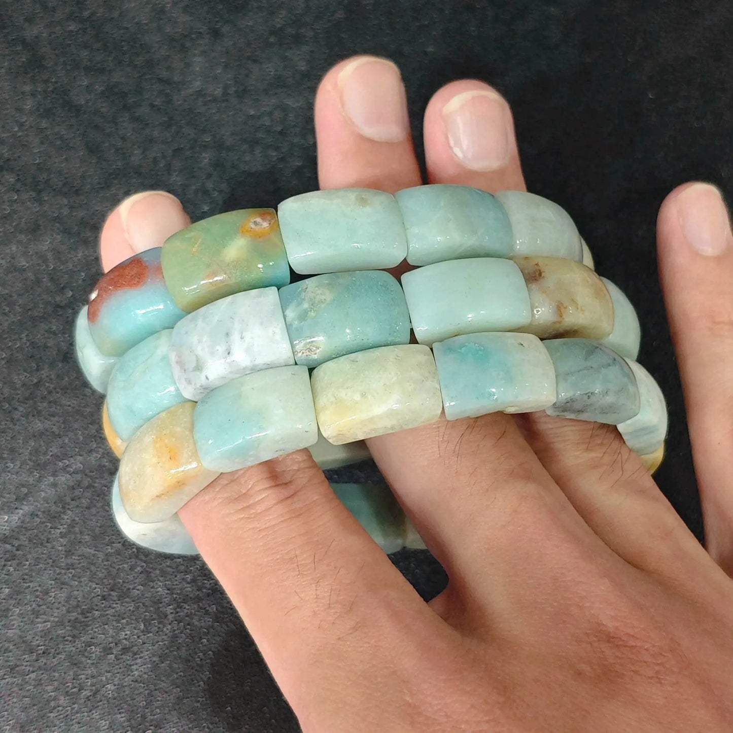 Stacked view of natural Caribbean Calcite rectangular tube bead bracelets worn over fingers displaying ocean blue tones